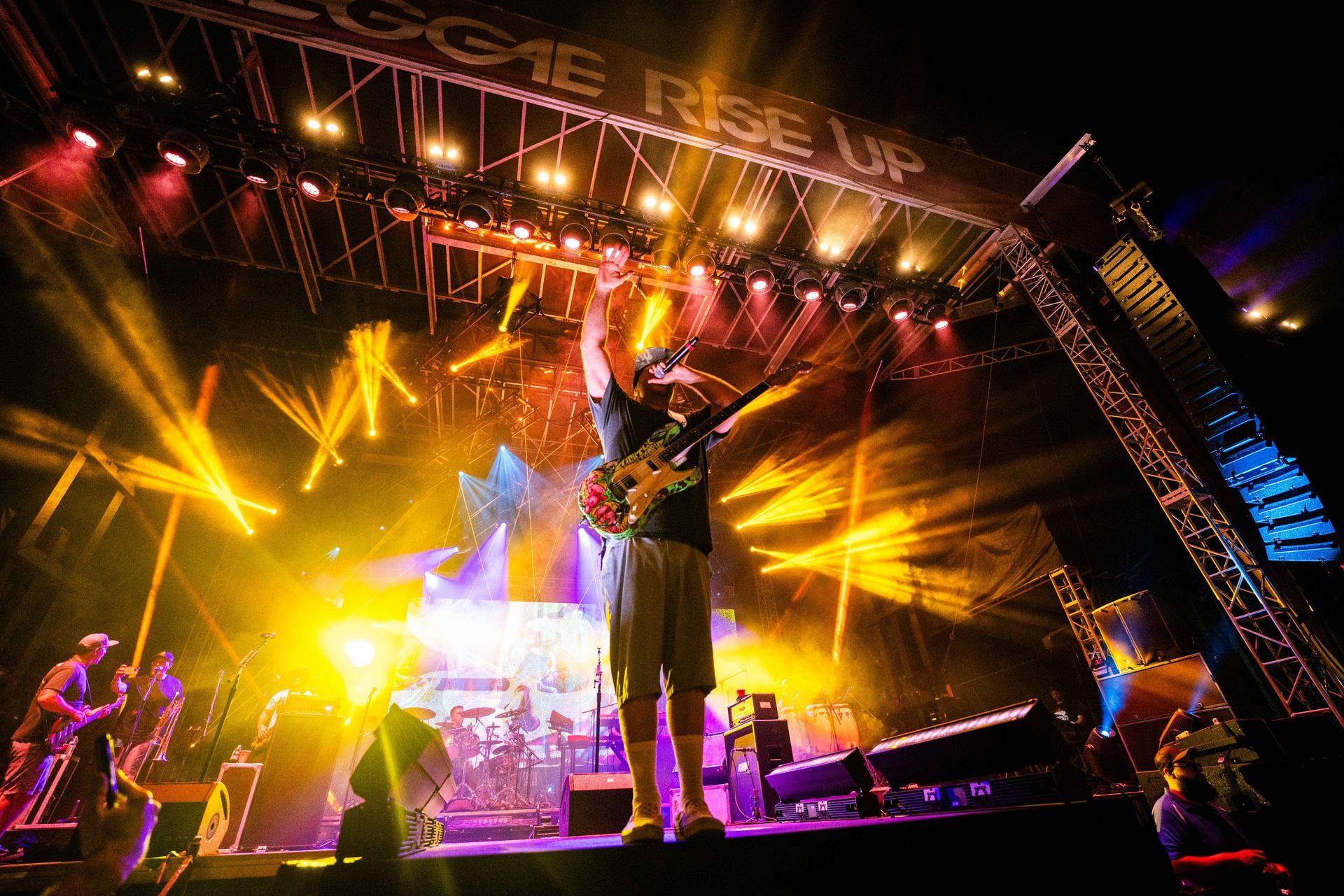 A man playing a guitar on a stage with a sign that says rise up