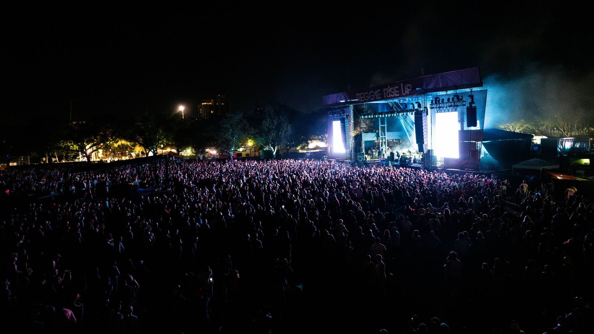 A large crowd of people are watching a concert at night.
