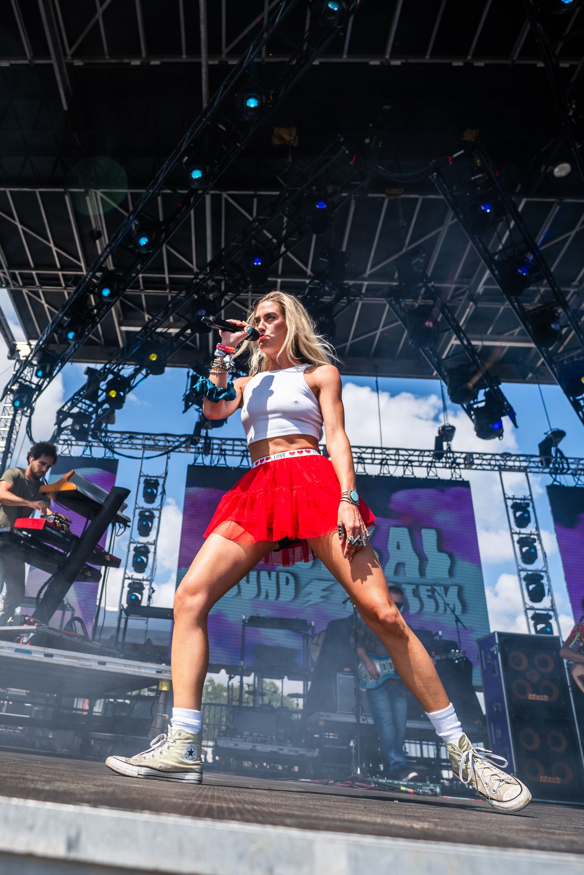 A woman in a red skirt is singing into a microphone on a stage.
