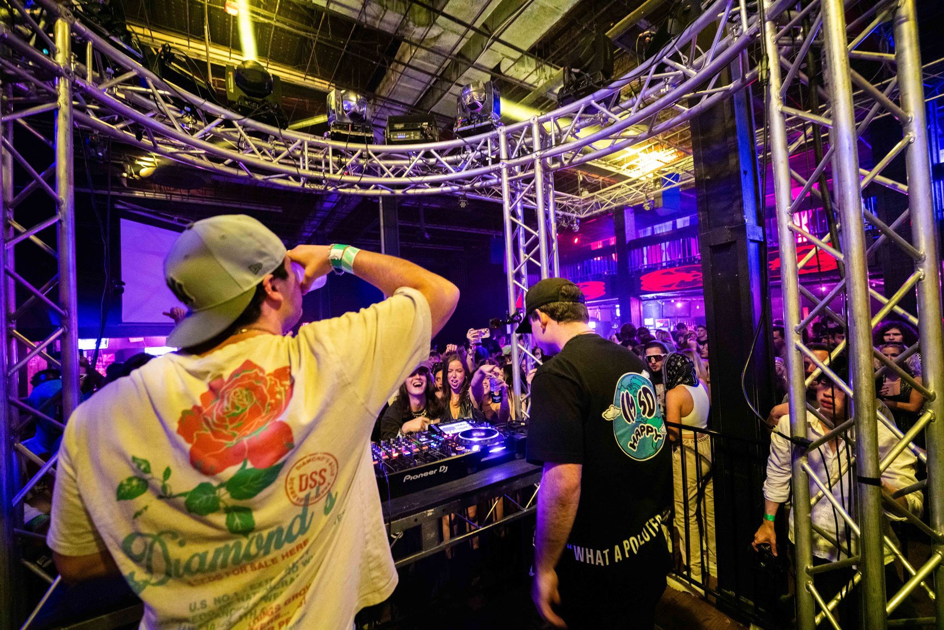 A man wearing a diamond t-shirt is standing in front of a dj booth.