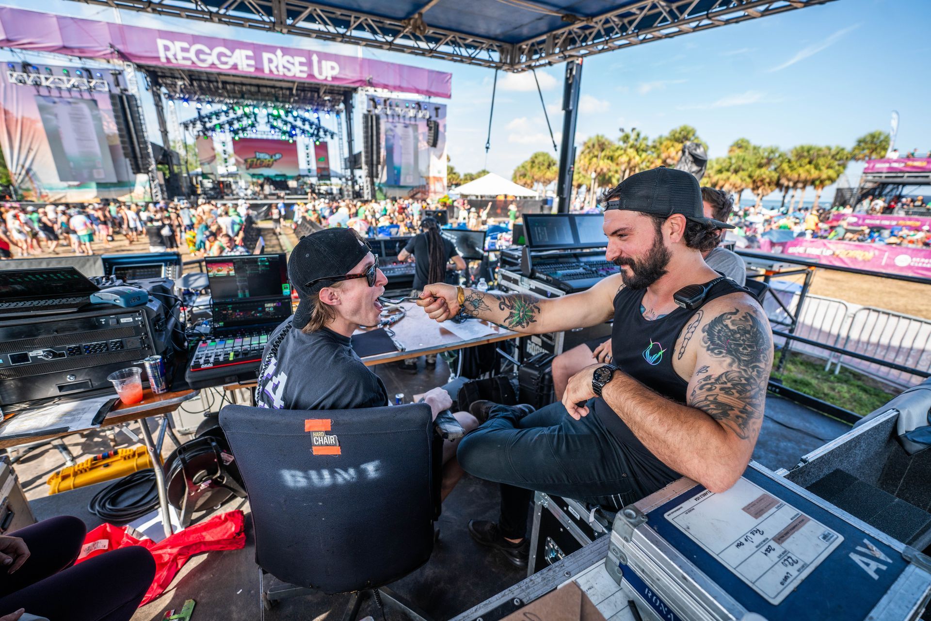 Two men are sitting at a table at a concert talking to each other.