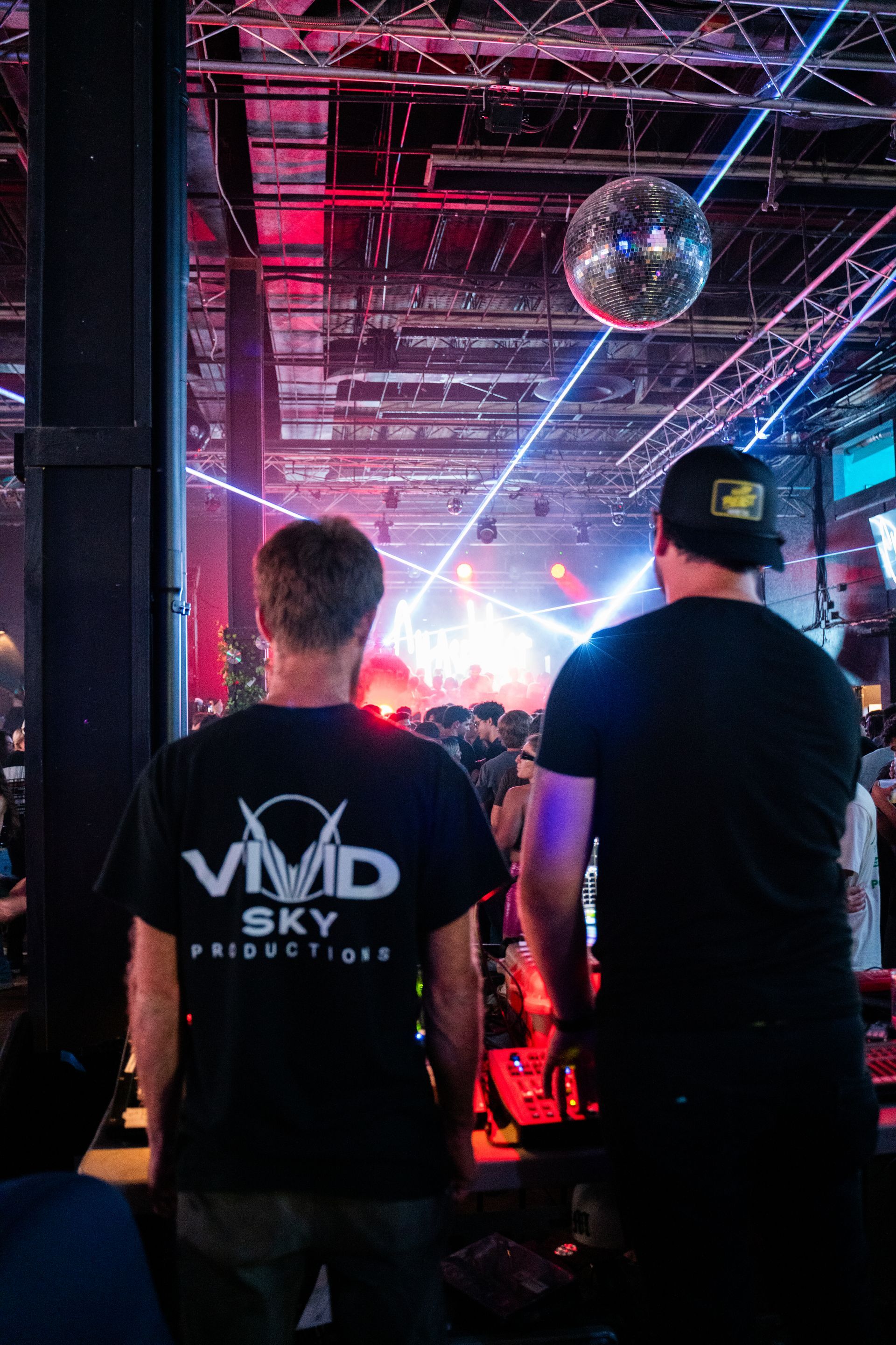 Two men are standing in a dark room with a disco ball hanging from the ceiling.