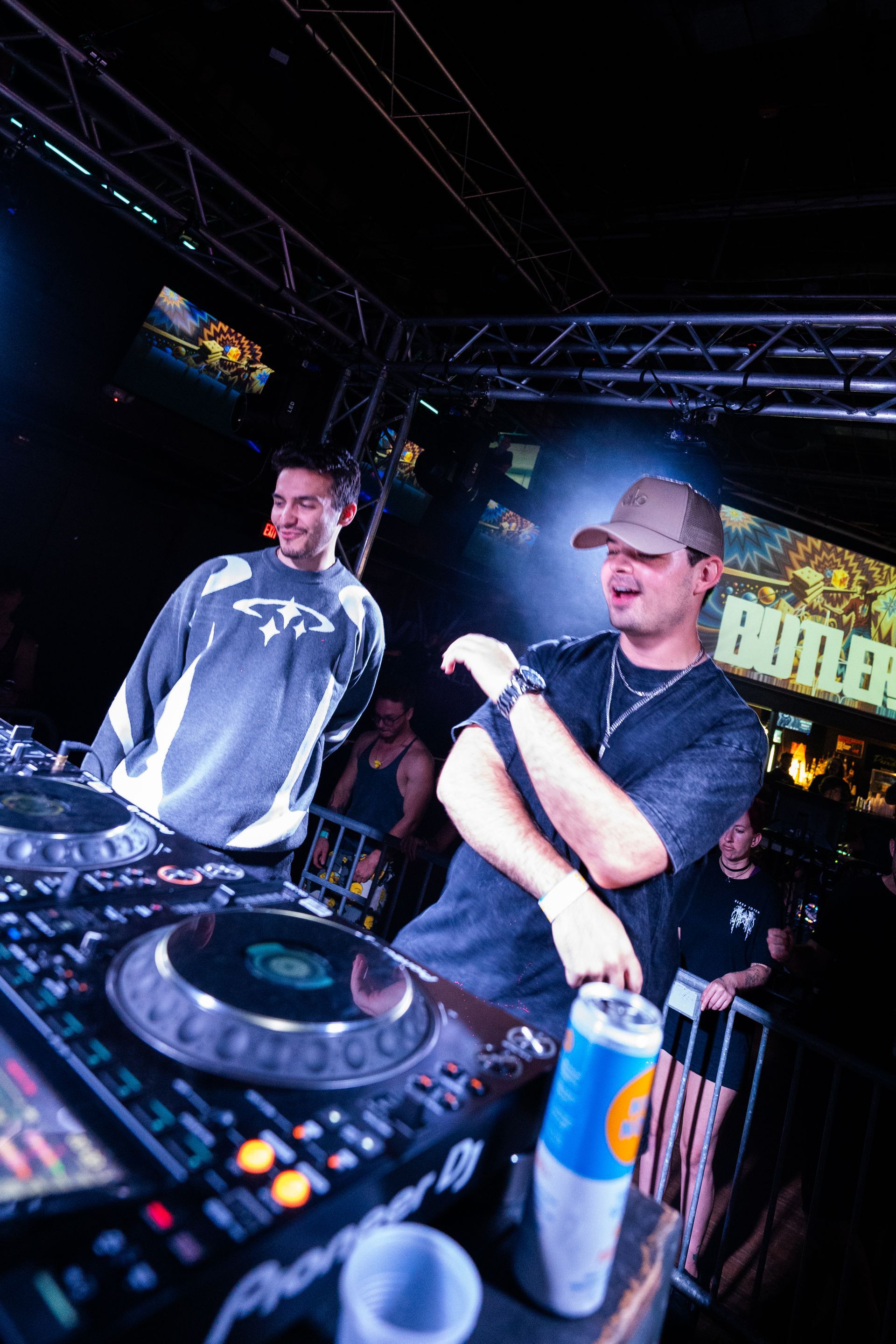 Two men are standing in front of a dj mixer in a club.