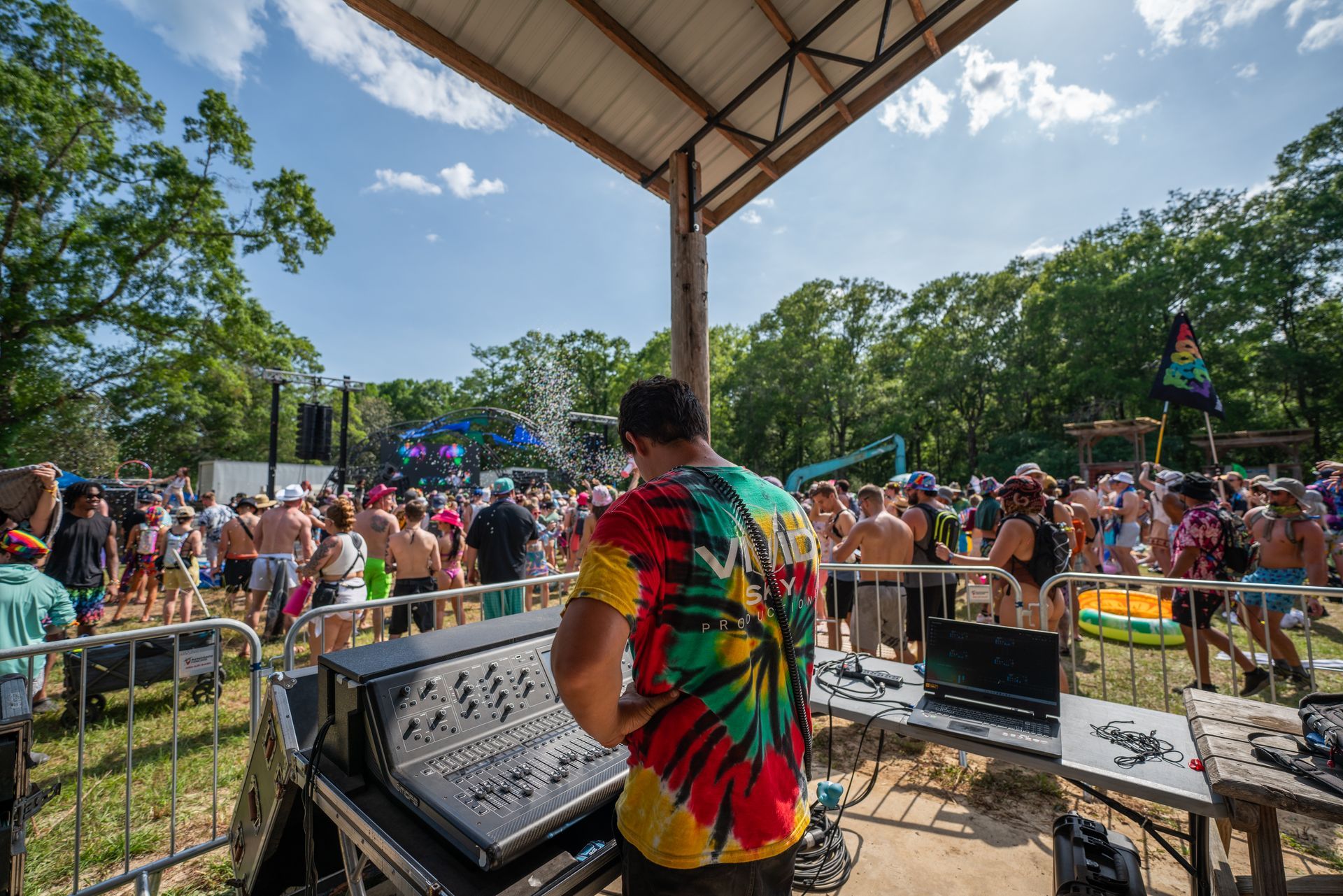 A man in a tie dye shirt is playing music in front of a crowd at a festival.