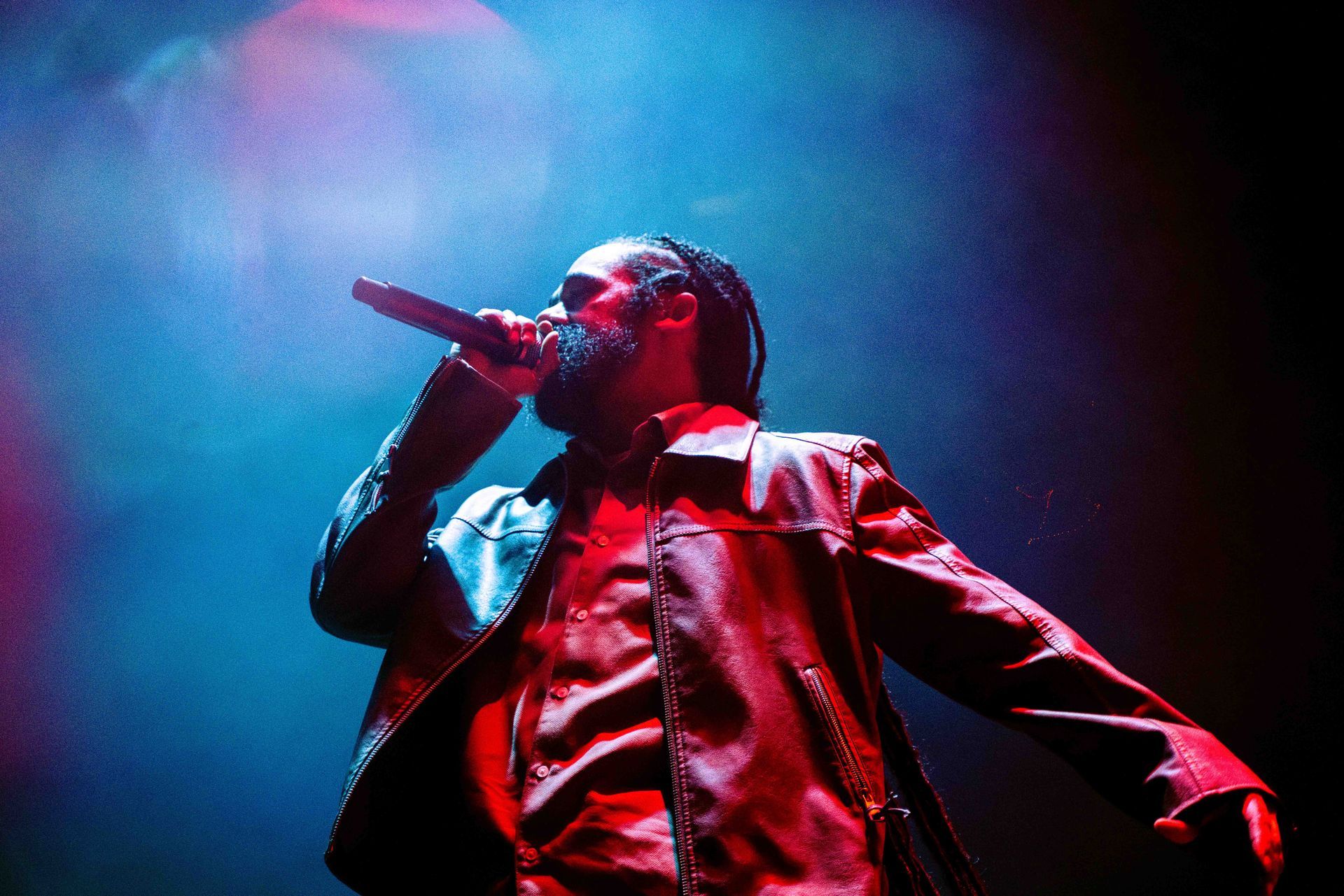 A man in a leather jacket is singing into a microphone on a stage.