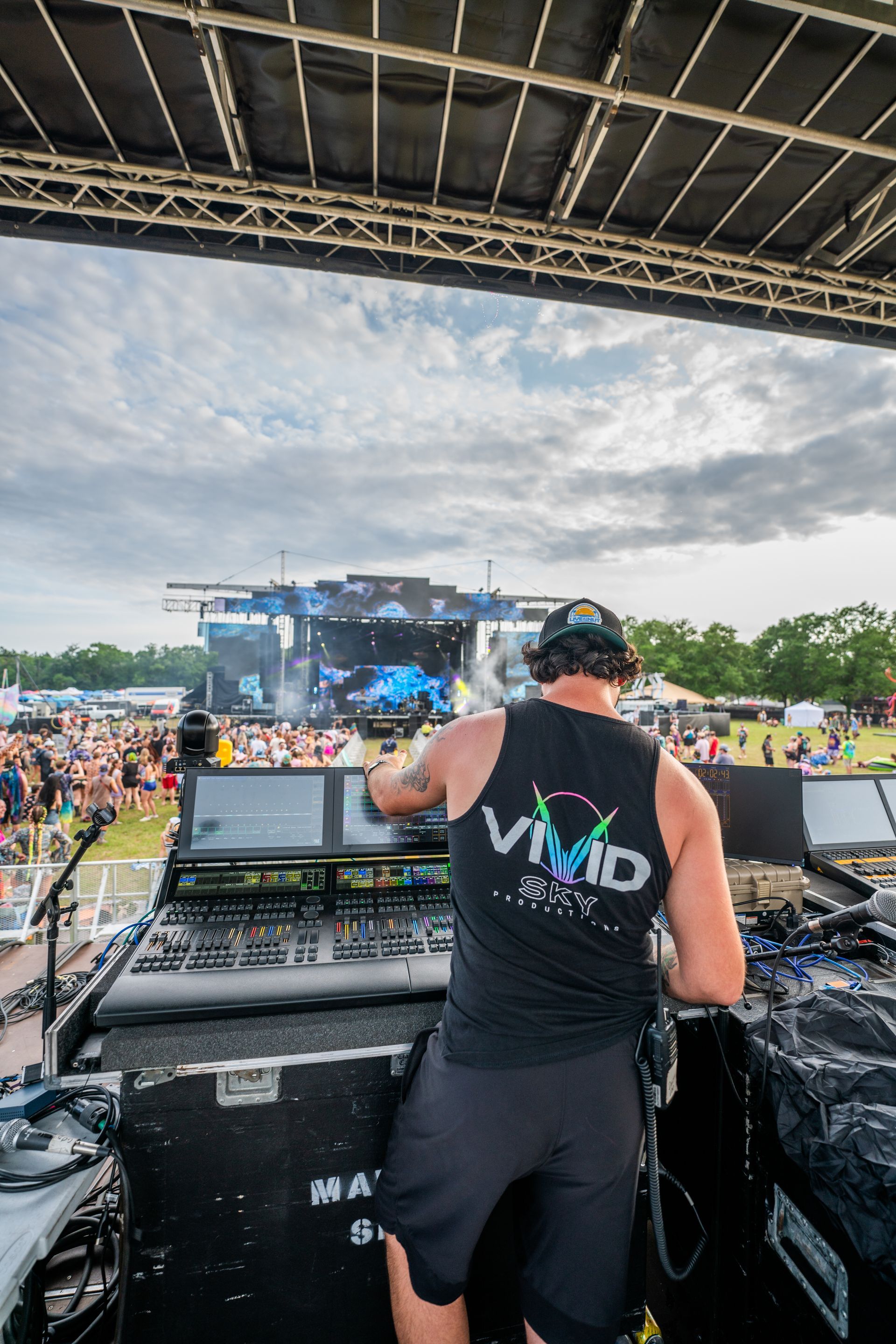 A man wearing a black tank top with the word vivid on it is standing in front of a stage.