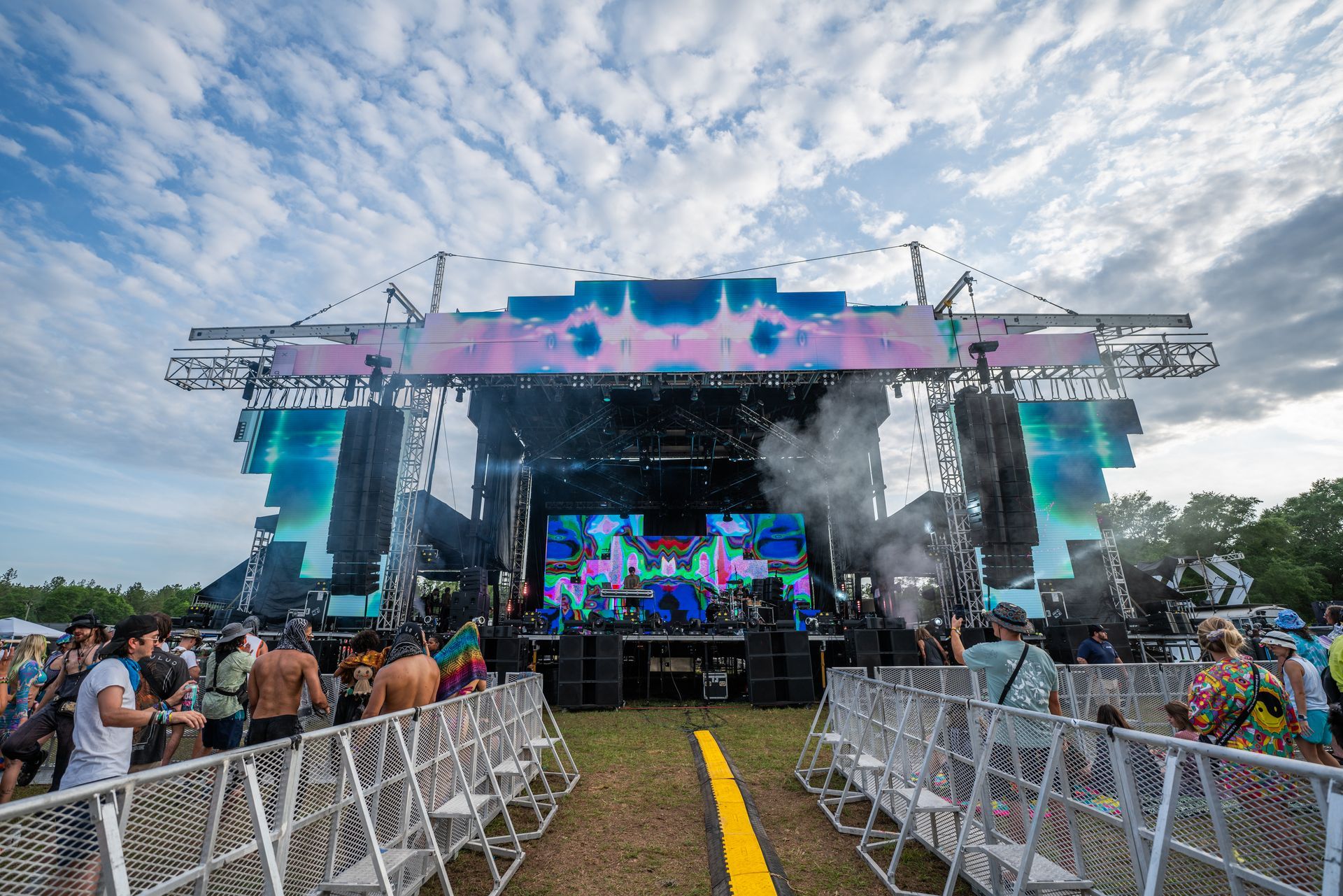 A large stage at a music festival with people standing around it.