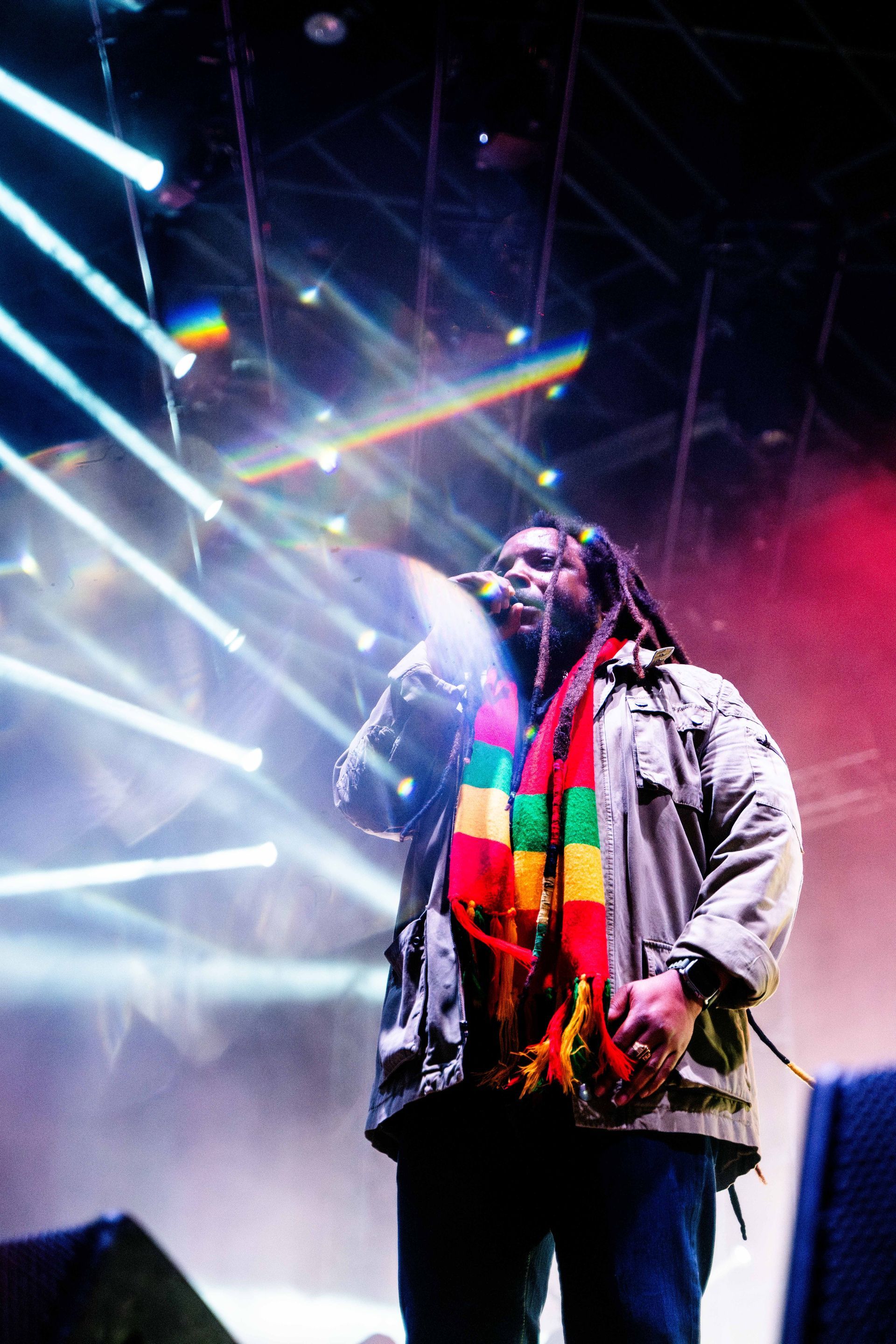A man with dreadlocks is singing into a microphone on a stage.