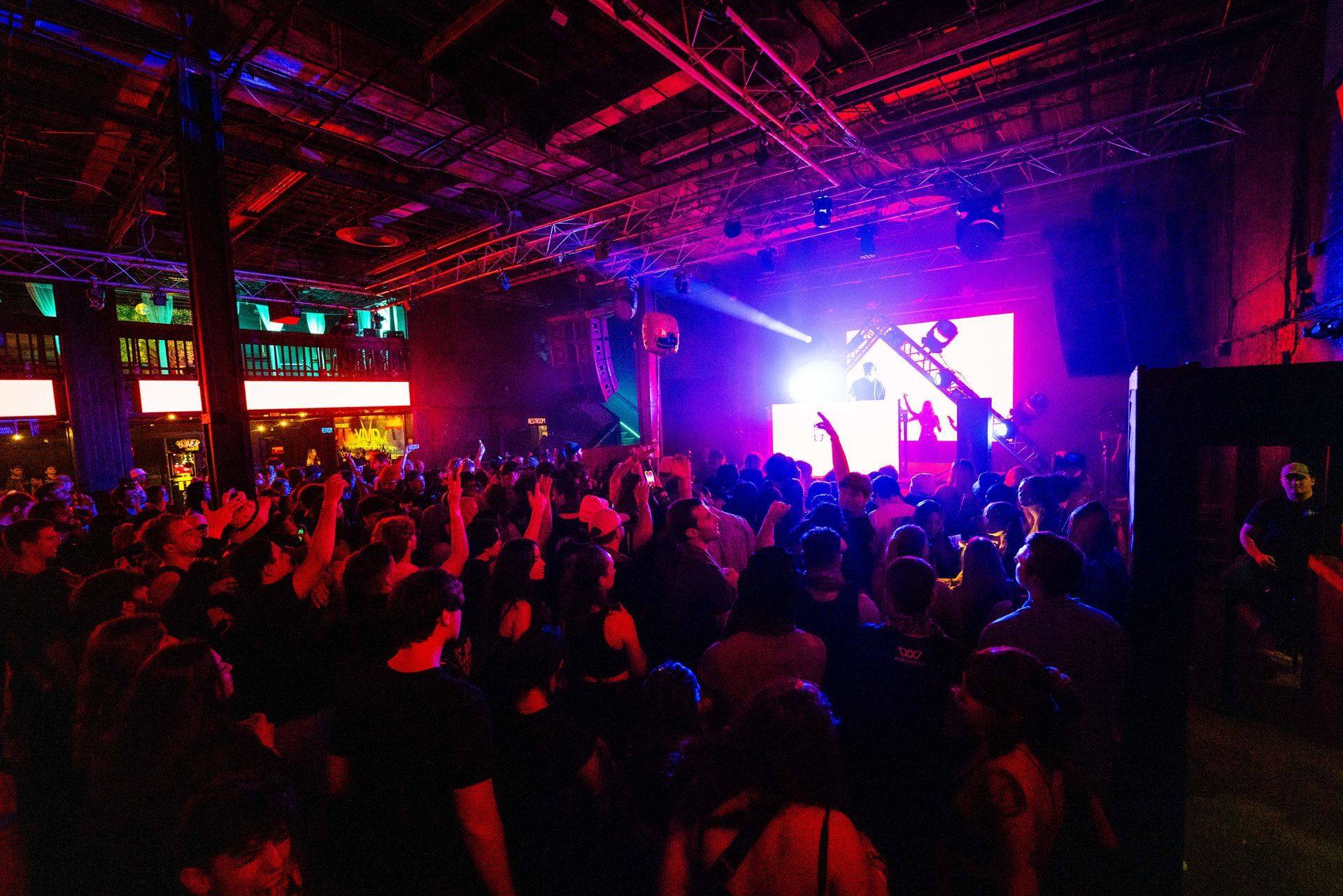 A crowd of people are dancing in a dark room with purple lights.