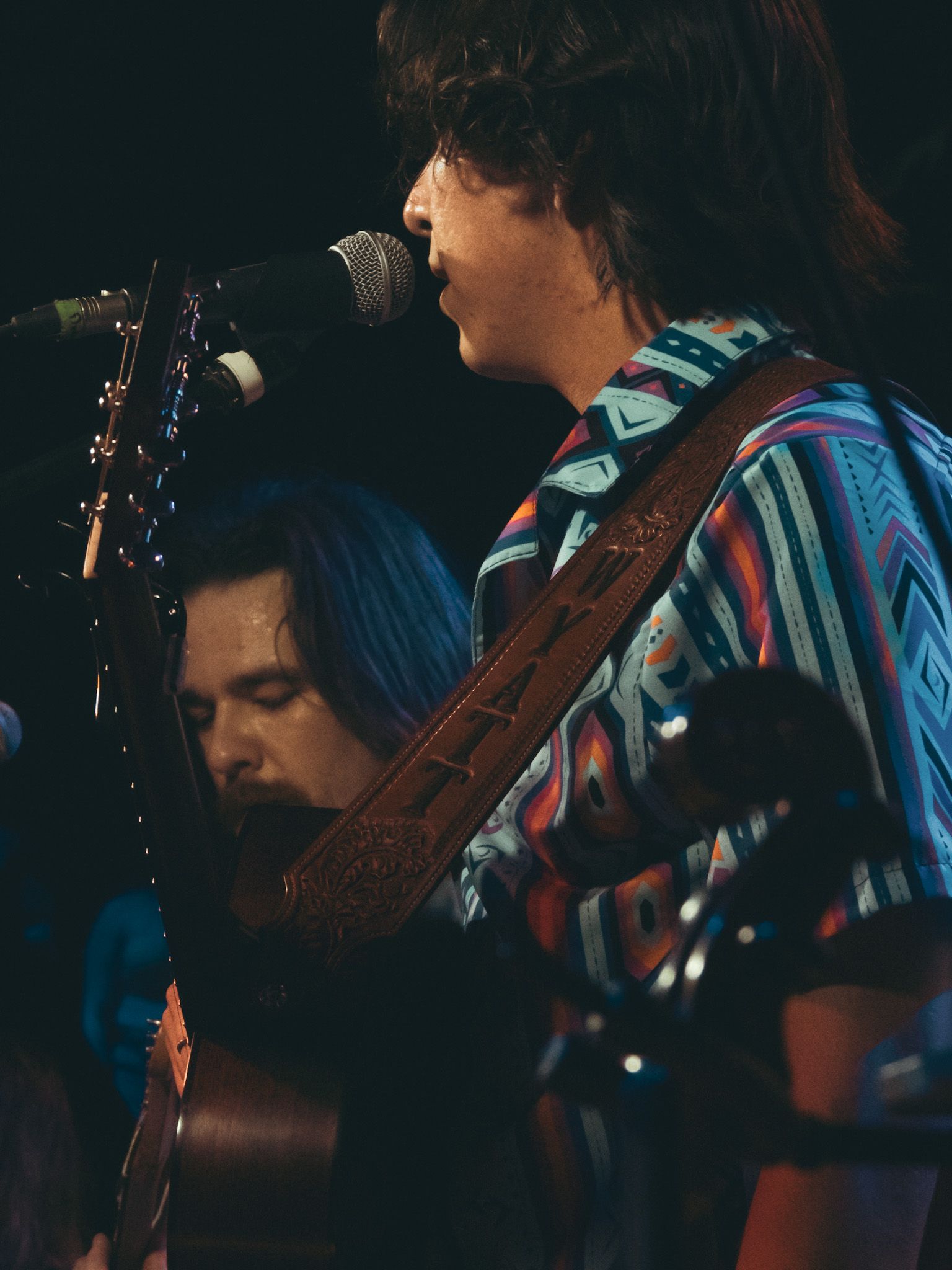 A man singing into a microphone while another man plays a guitar