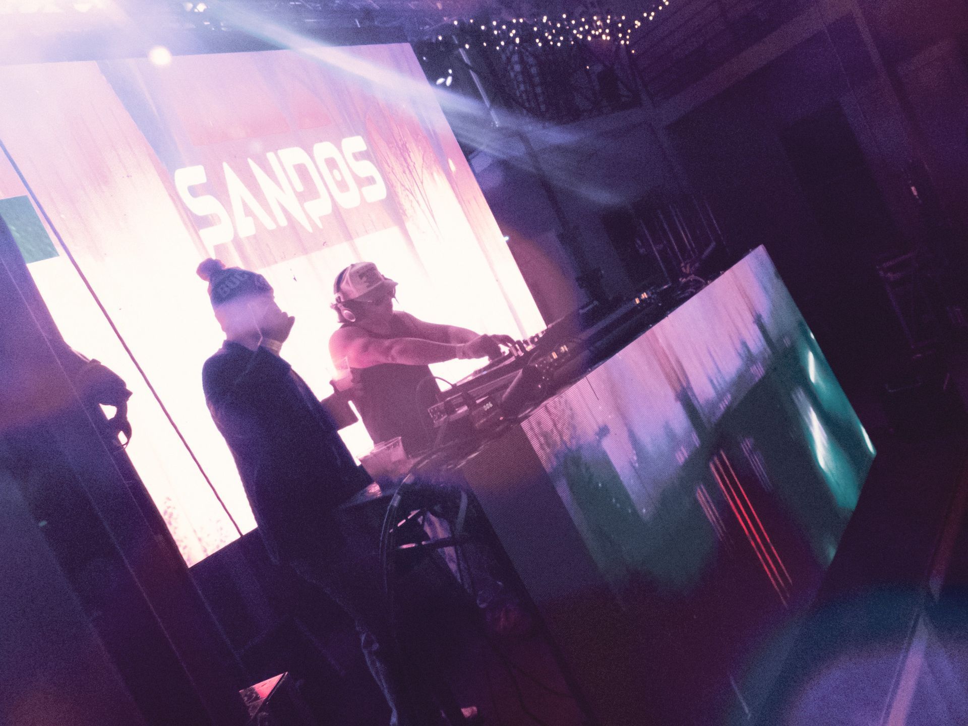 Two people are playing music in front of a screen that says sandos