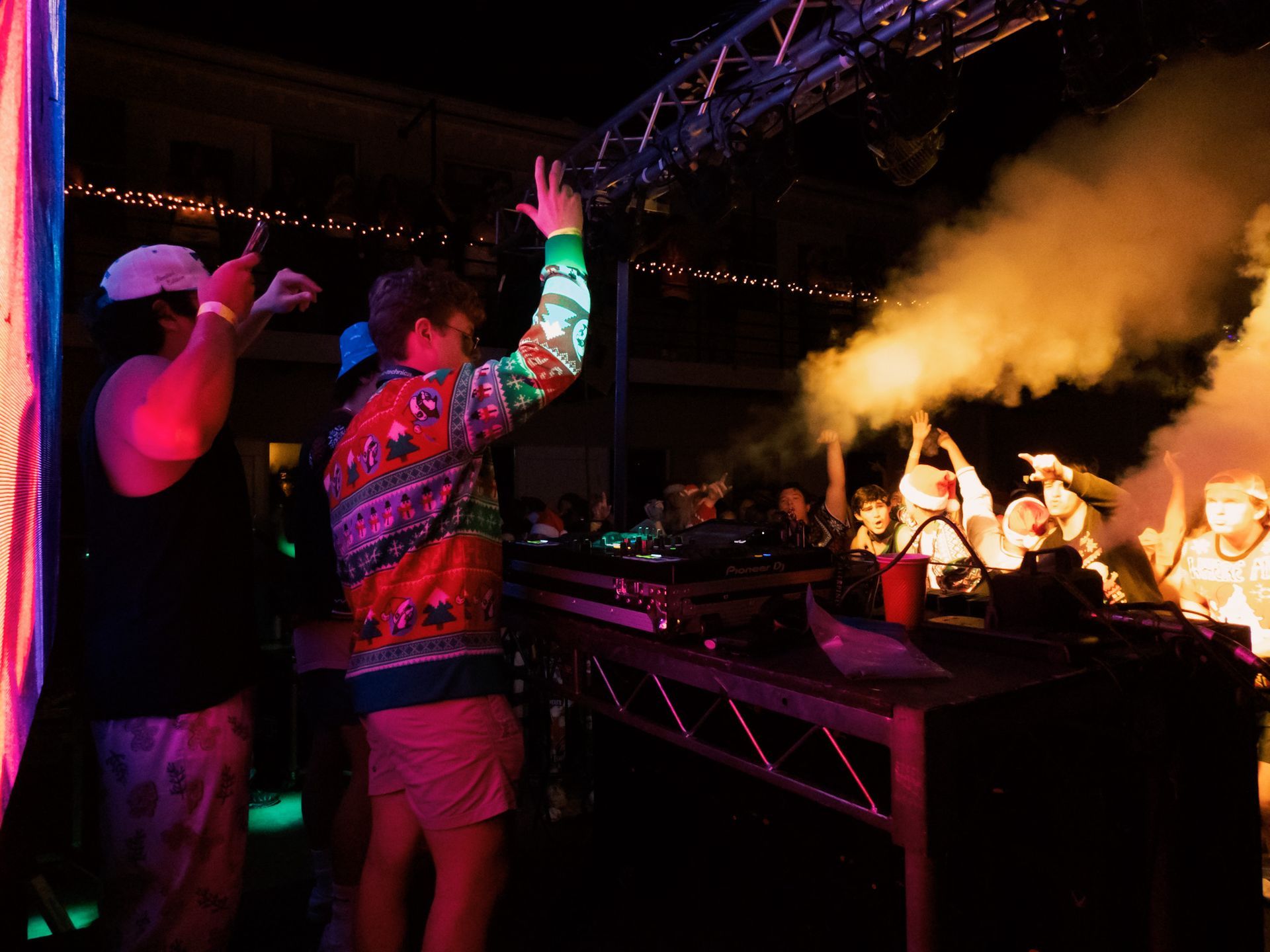 A group of people are standing in front of a dj at a party.