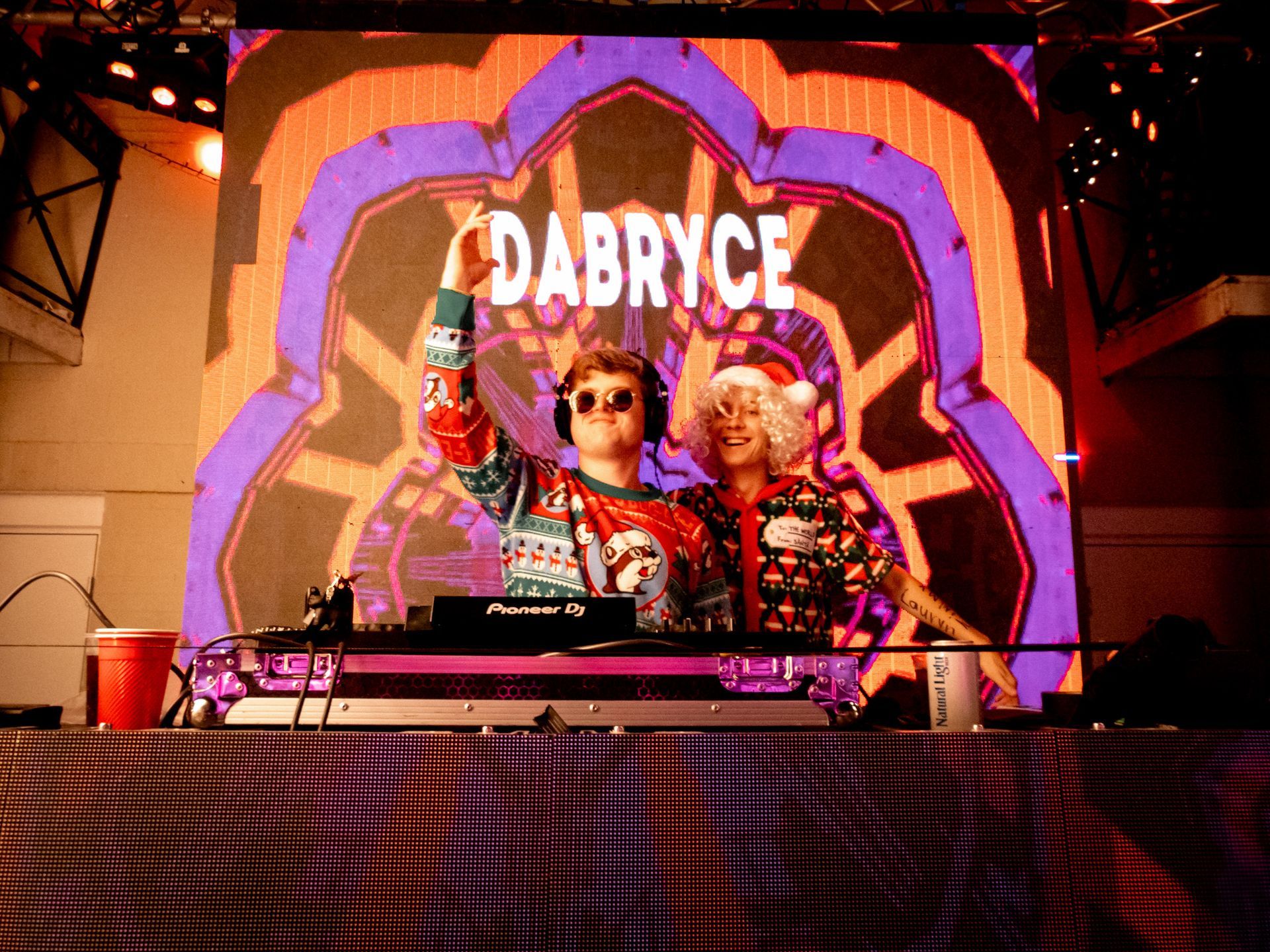 Two djs are standing in front of a large screen that says dabryce