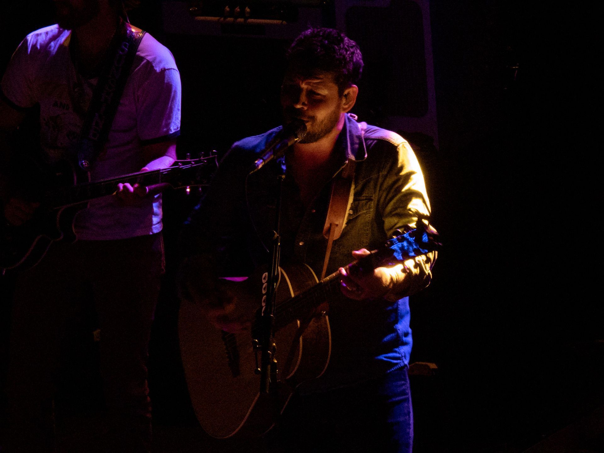 A man is playing a guitar and singing into a microphone on a stage.
