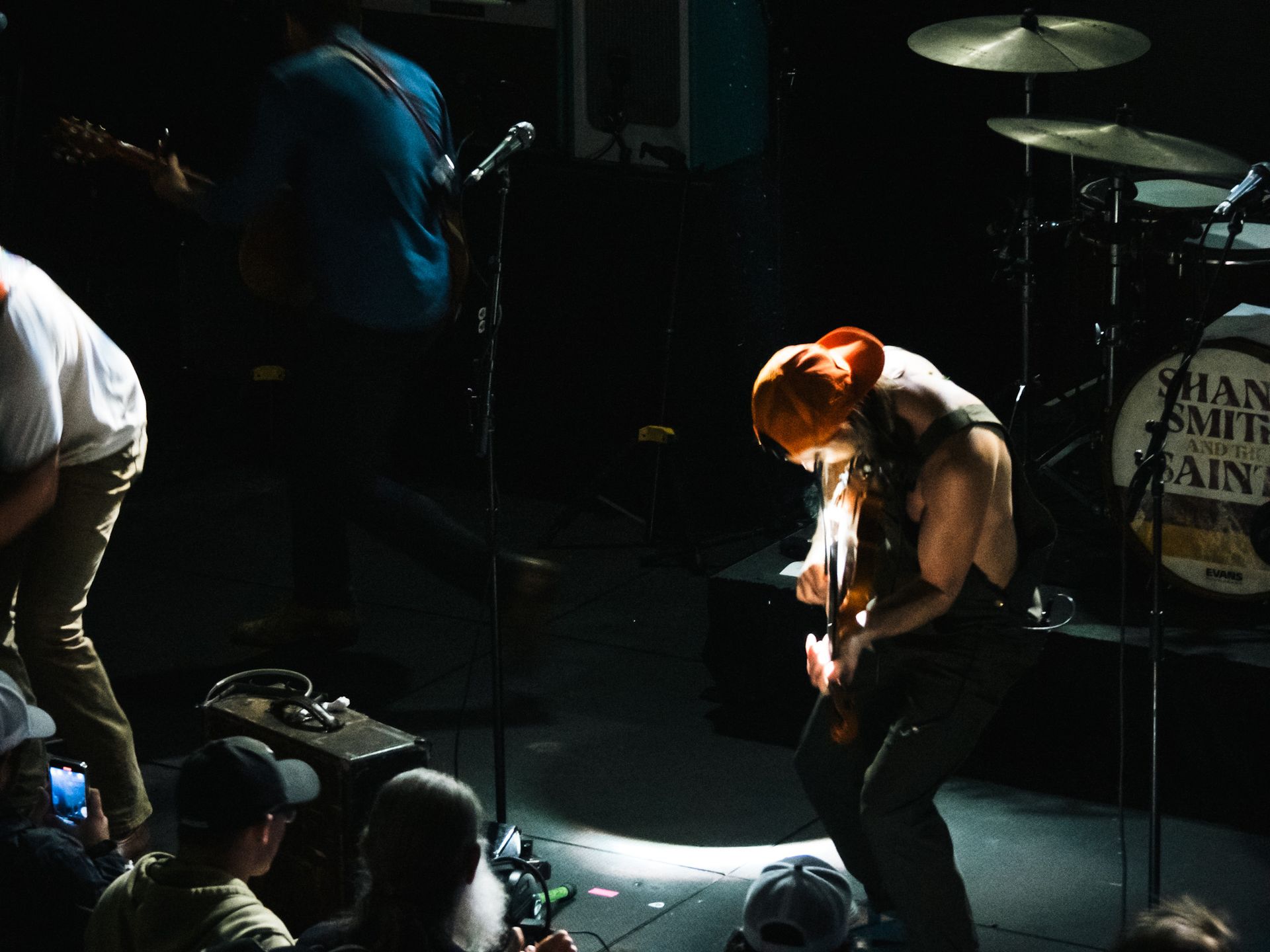 A man playing a guitar in front of a drum set that says ' man smith ' on it