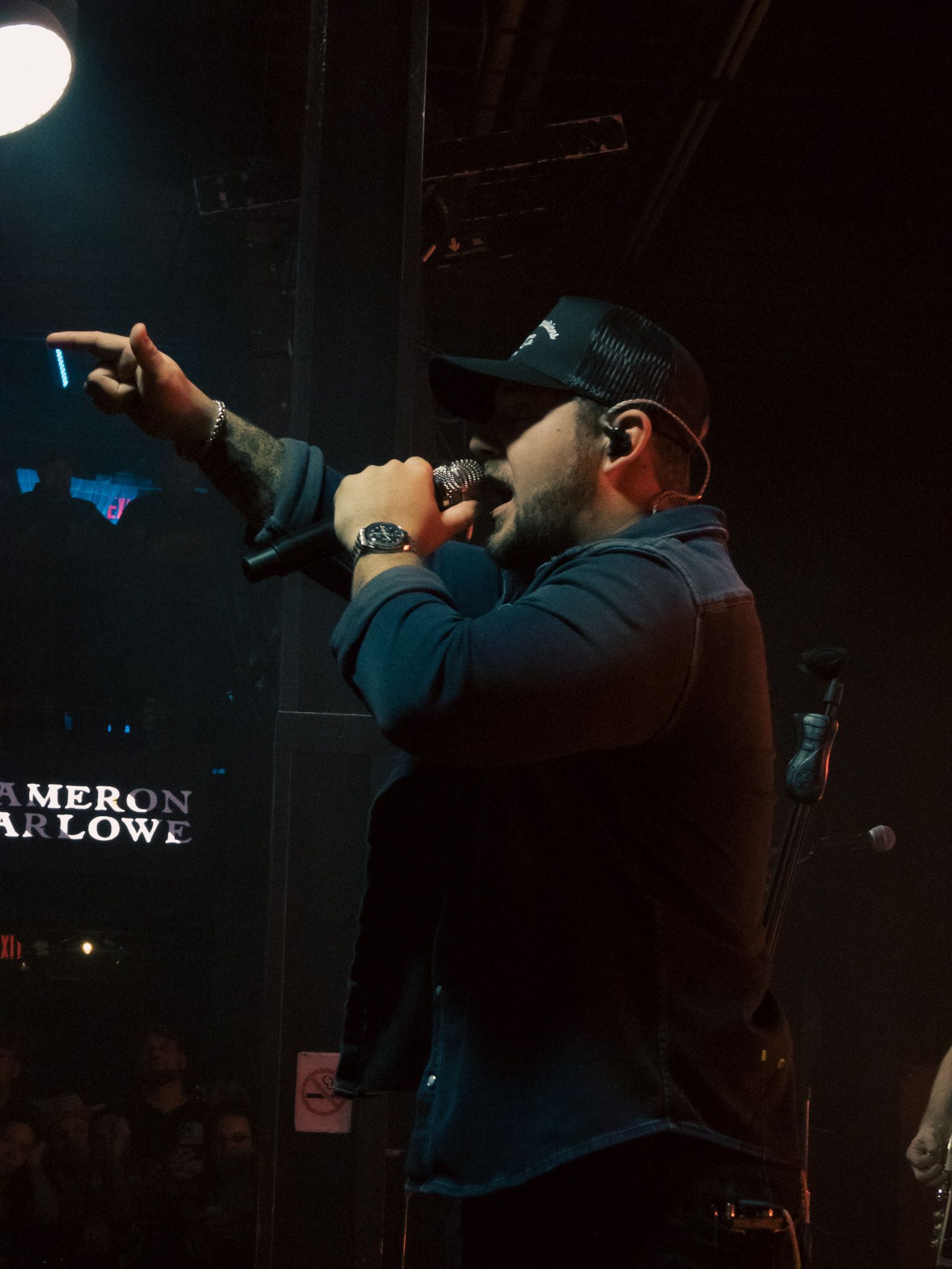 A man singing into a microphone in front of a sign that says cameron arrow