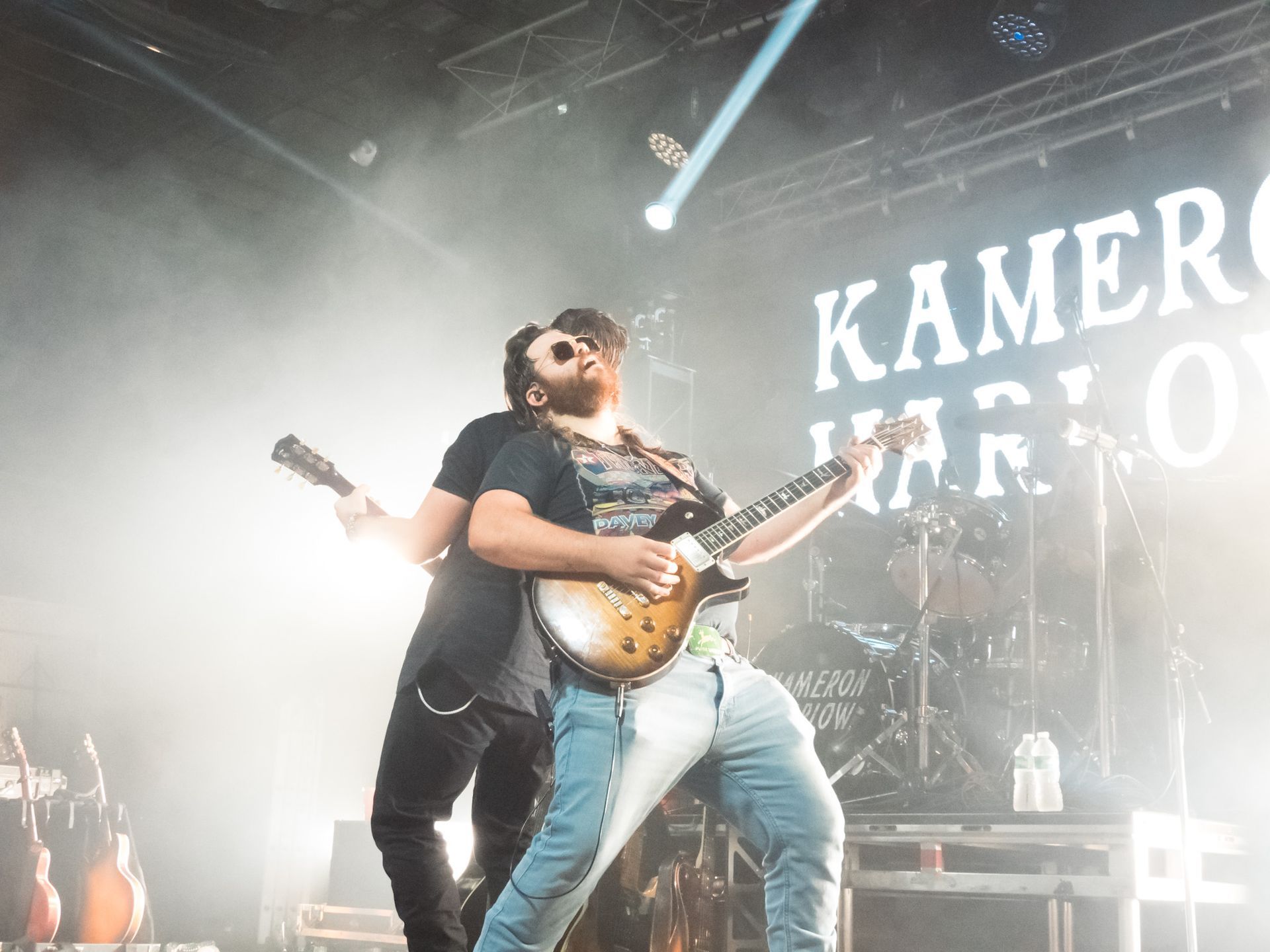 A man is playing a guitar on stage in front of a sign that says kamero