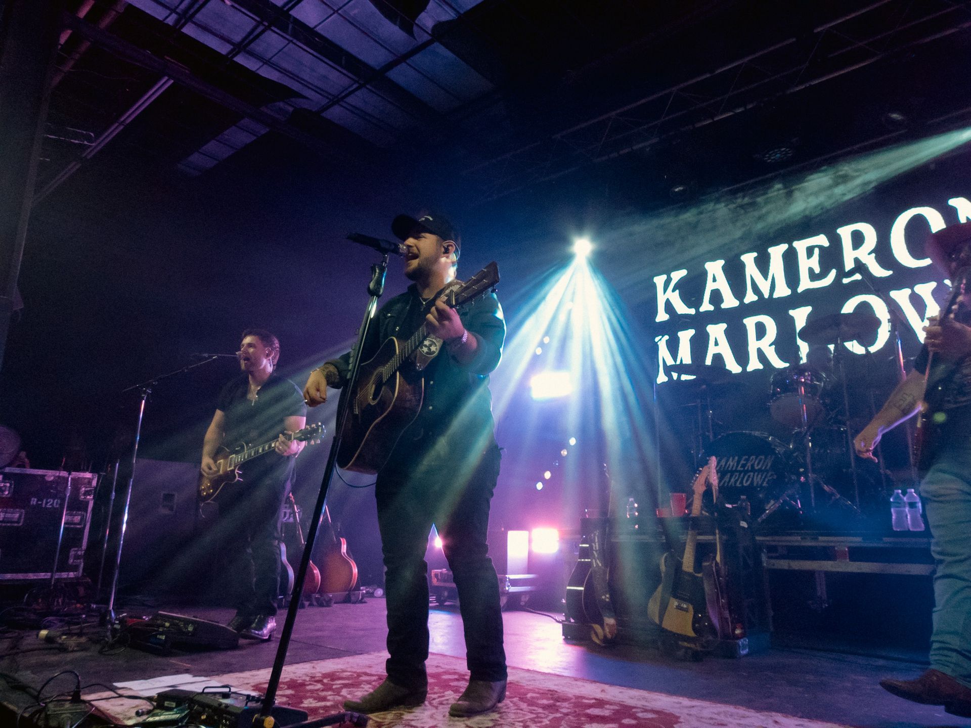 A man singing into a microphone in front of a sign that says kameron marlow