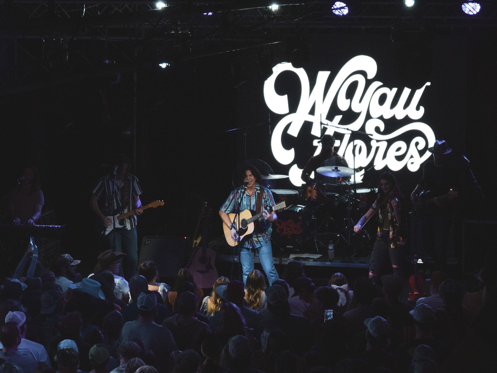 A man playing a guitar on stage in front of a sign that says w.you jones