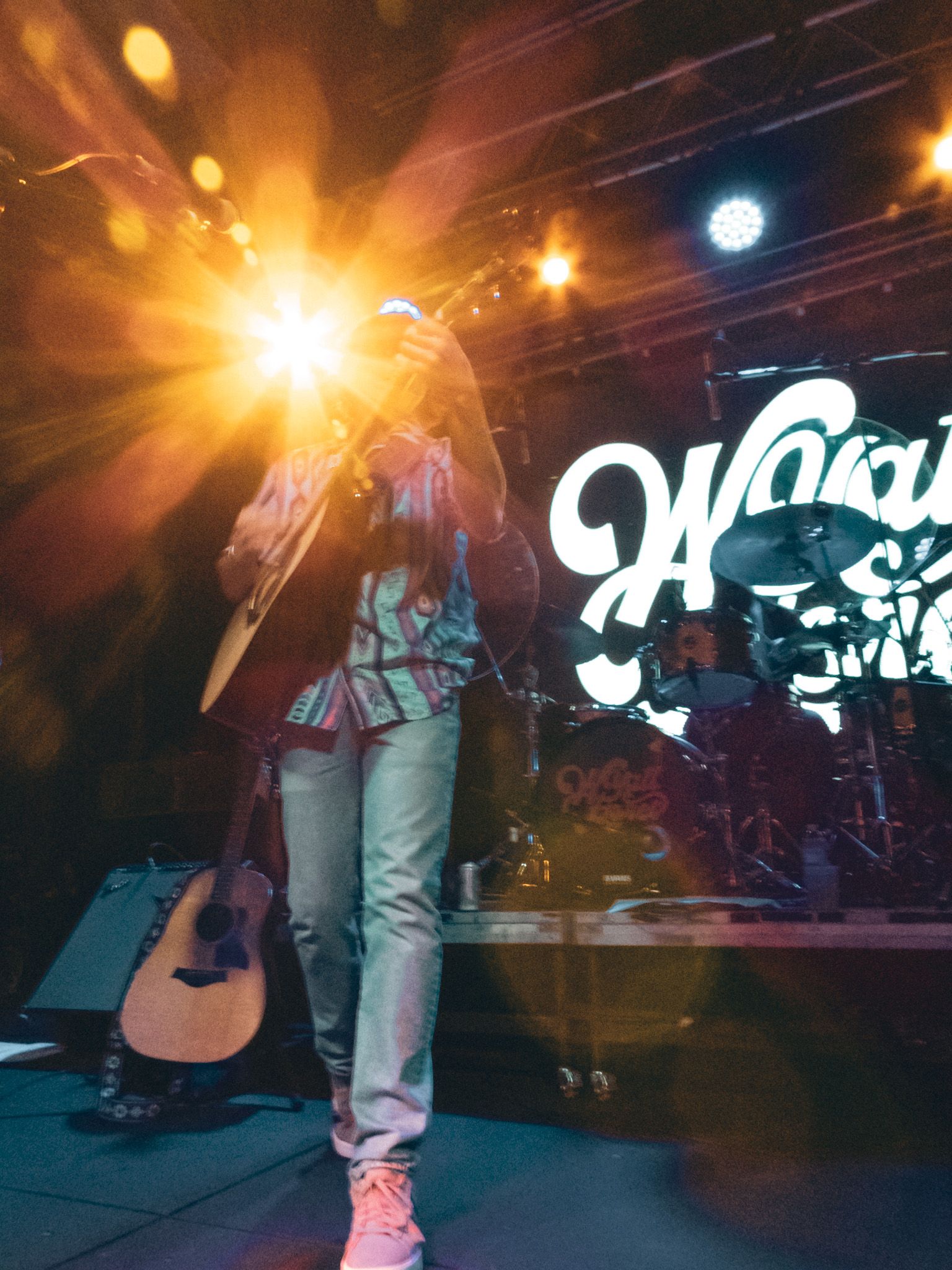 A man is playing a guitar on a stage in front of a sign that says ' hawaii '