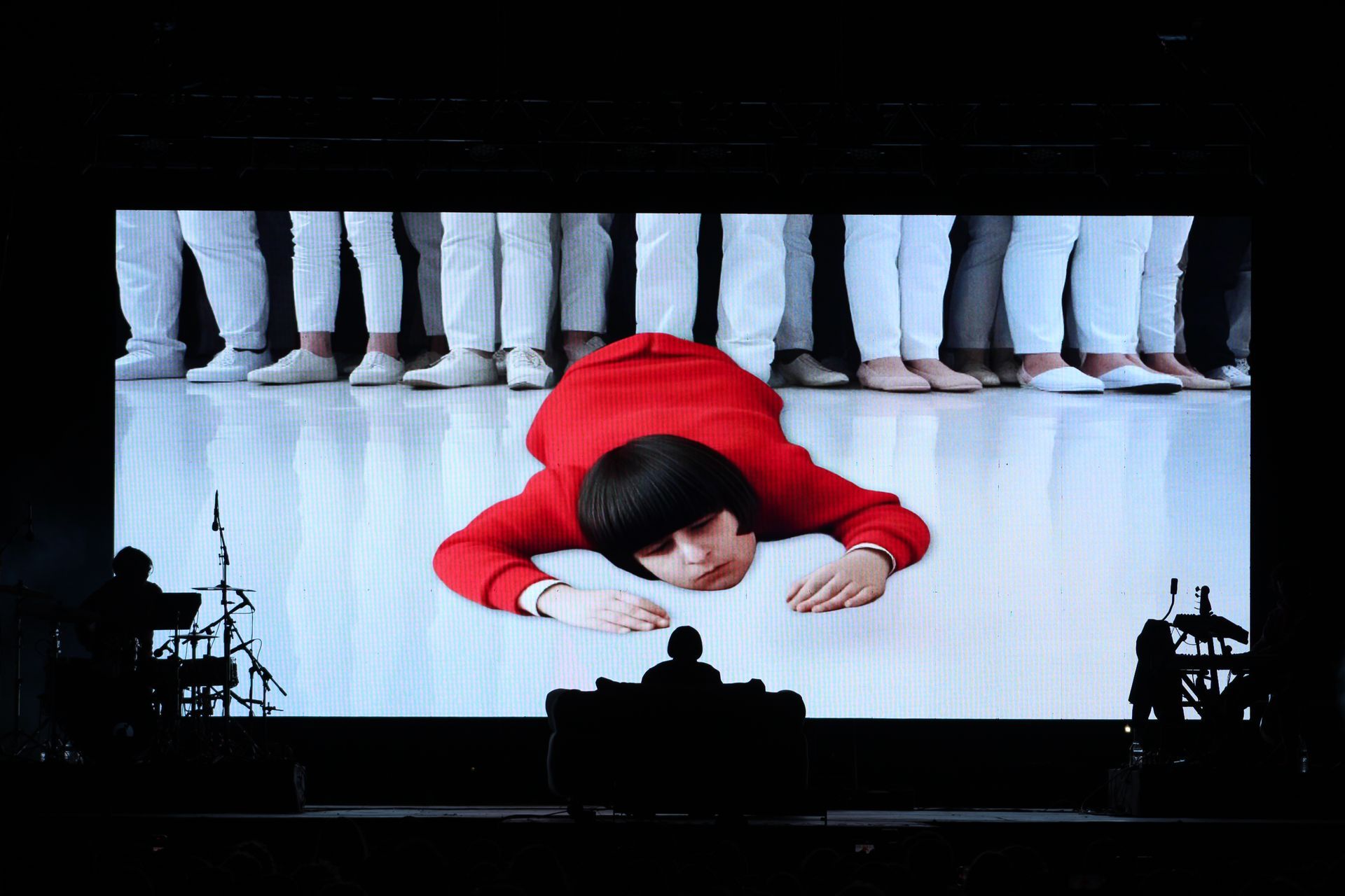 A woman in a red sweater is laying on the floor in front of a group of people in white pants.