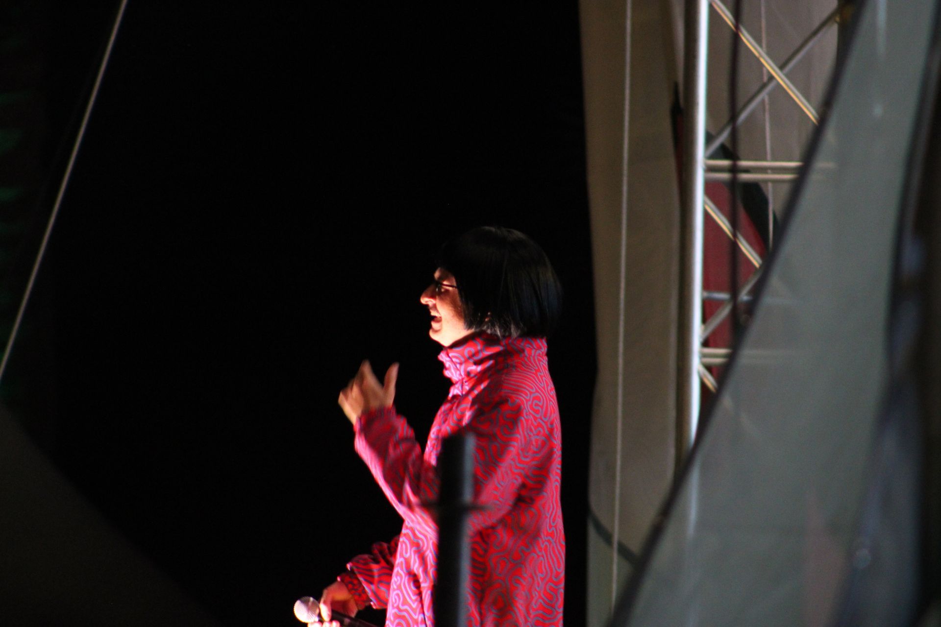 A woman in a pink jacket is standing in front of a black curtain.