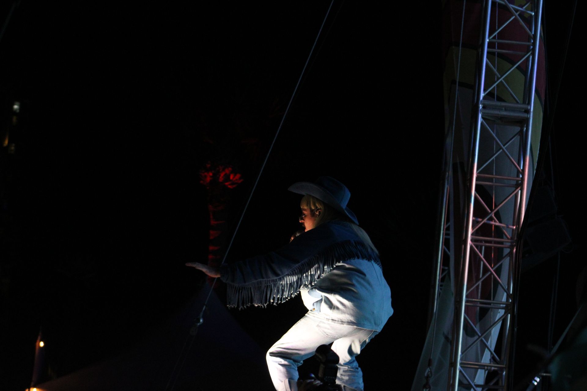 A man in a hat is standing on a stage in the dark.