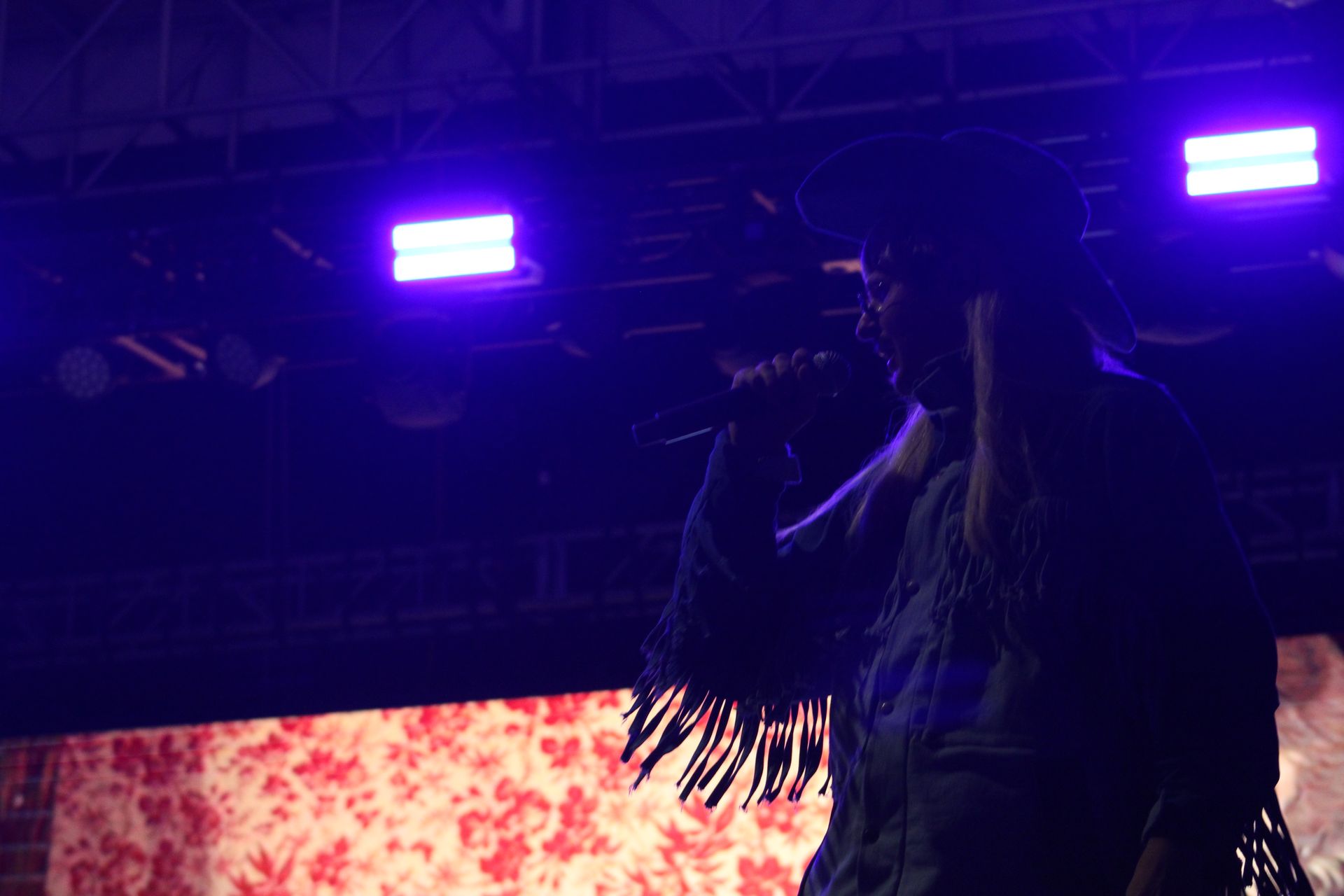 A woman is singing into a microphone on a stage with purple lights.