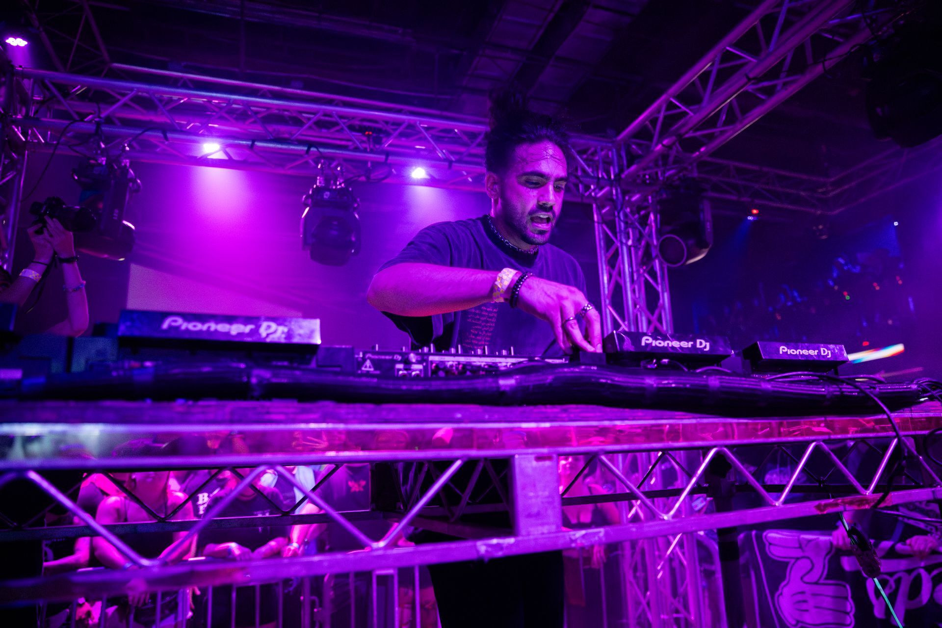 A man is playing a dj set in a dark room with purple lights.