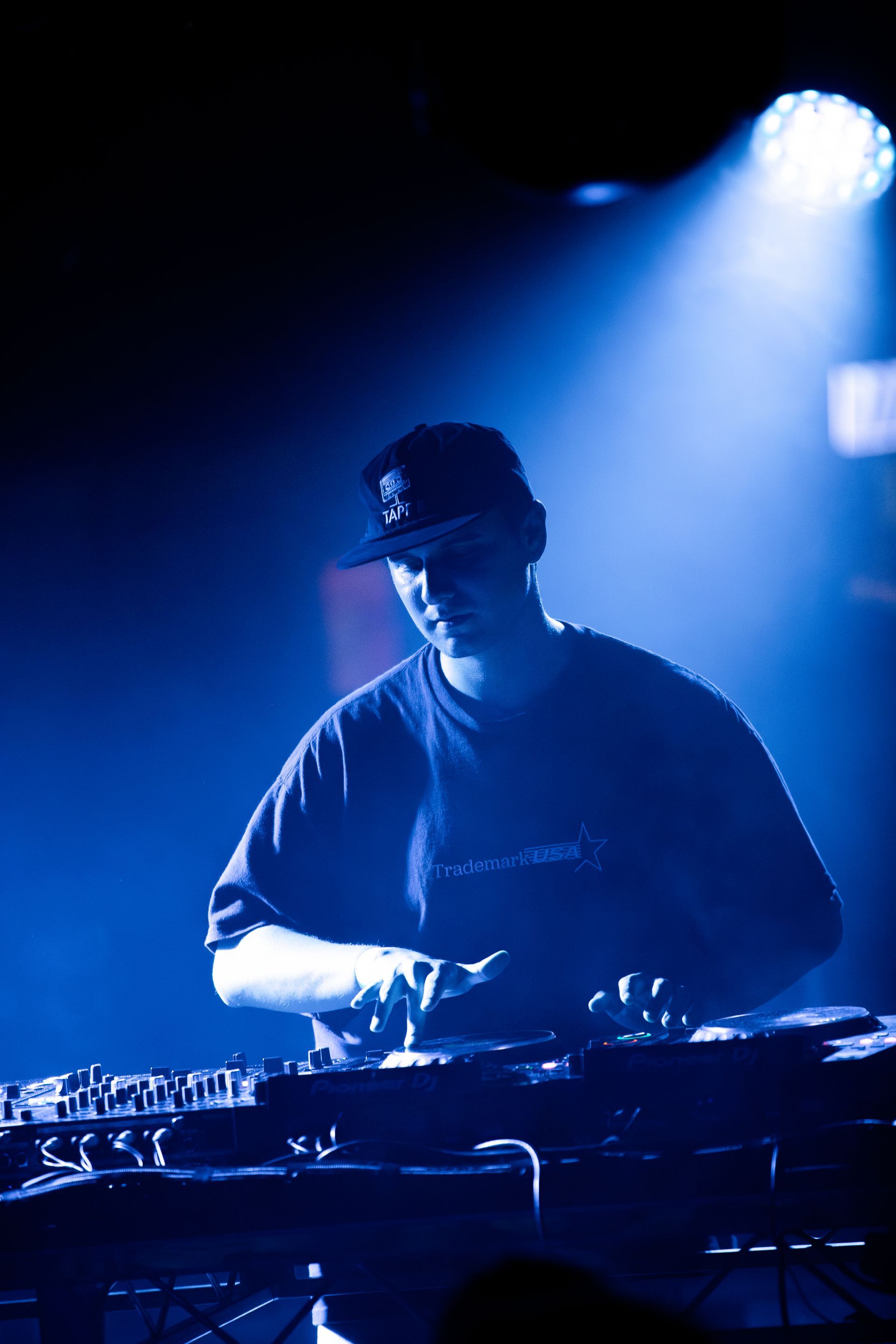 A man in a hat is playing a dj set in a dark room.