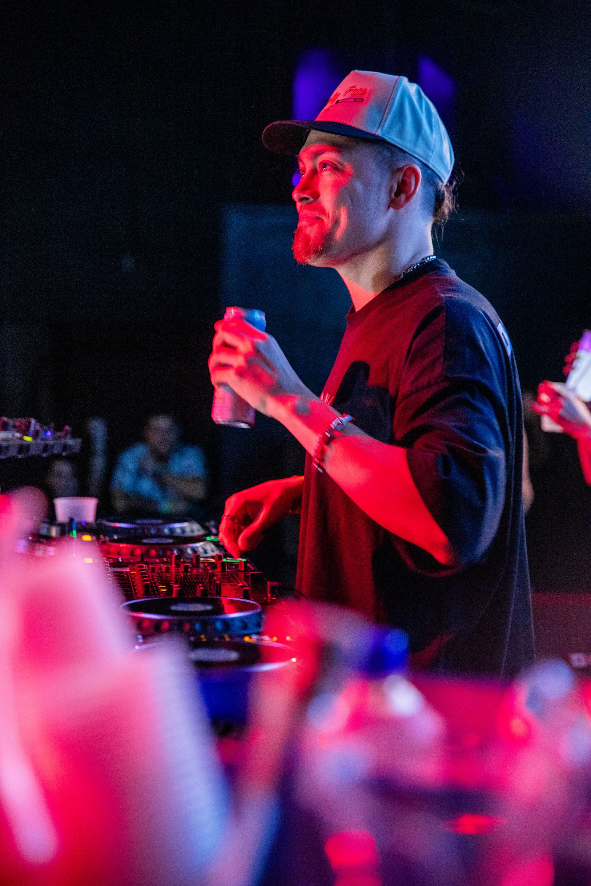 A man in a hat is holding a can of soda in a dark room.