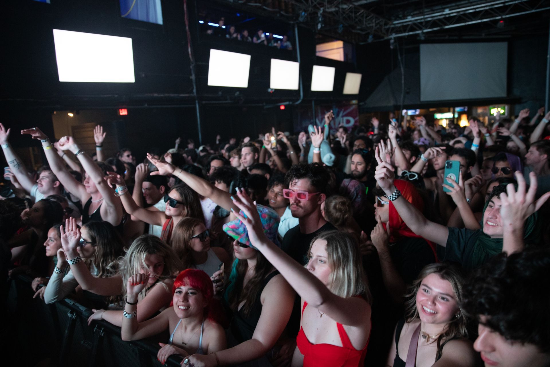 A crowd of people are standing in a dark room with their hands in the air.