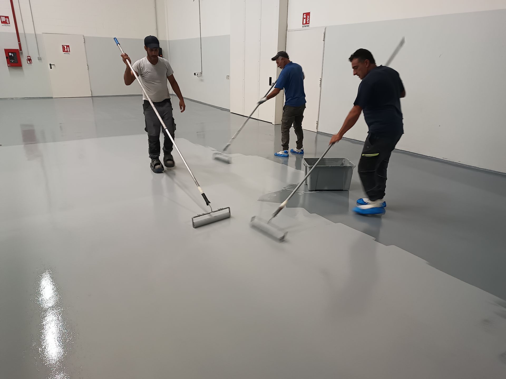 Tre uomini stanno dipingendo un pavimento con rulli e stracci