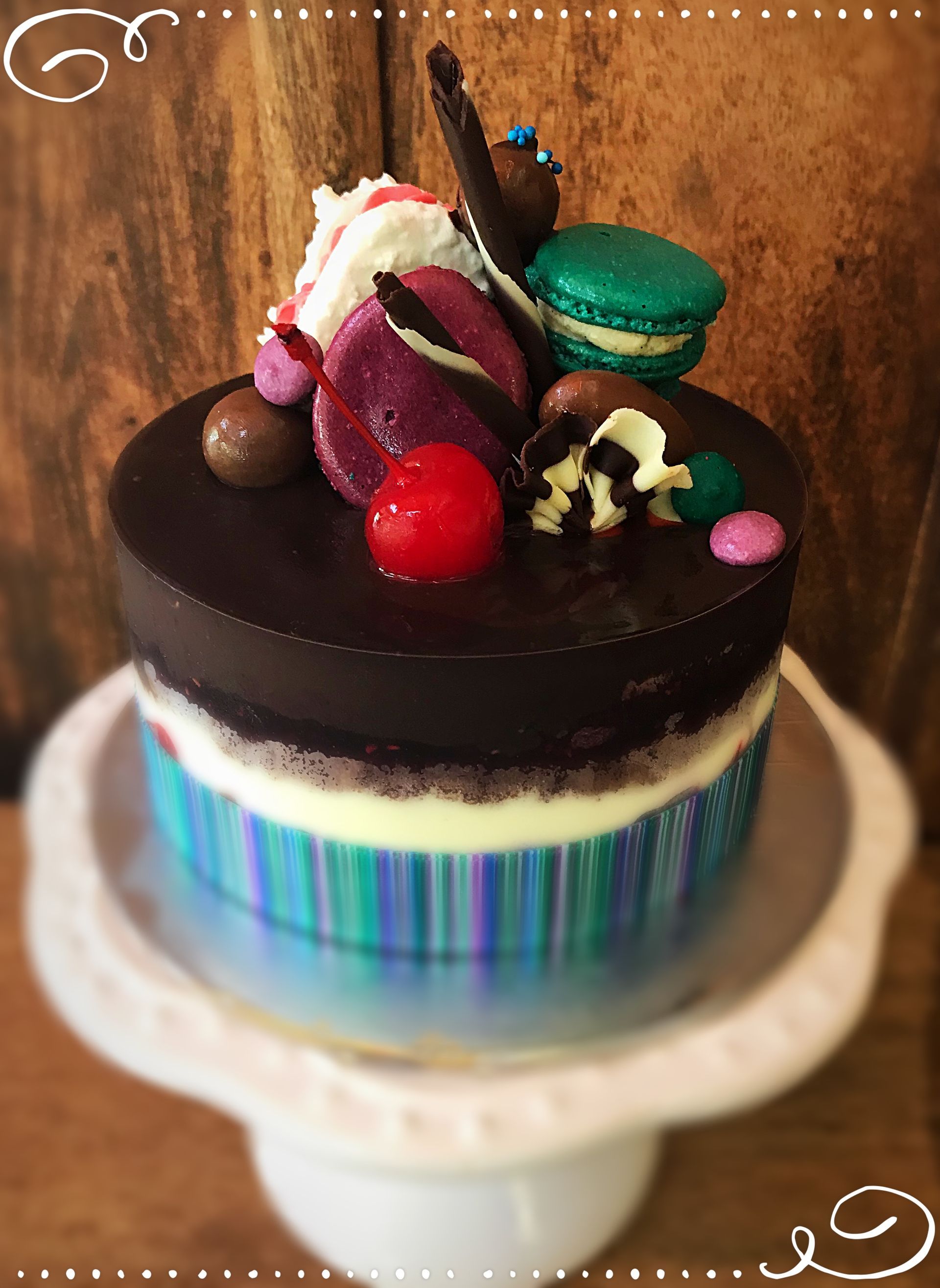 A chocolate cake with macarons and cherries on top — My Rainbow Bakery, Cafe & Catering in Cannonvale, QLD