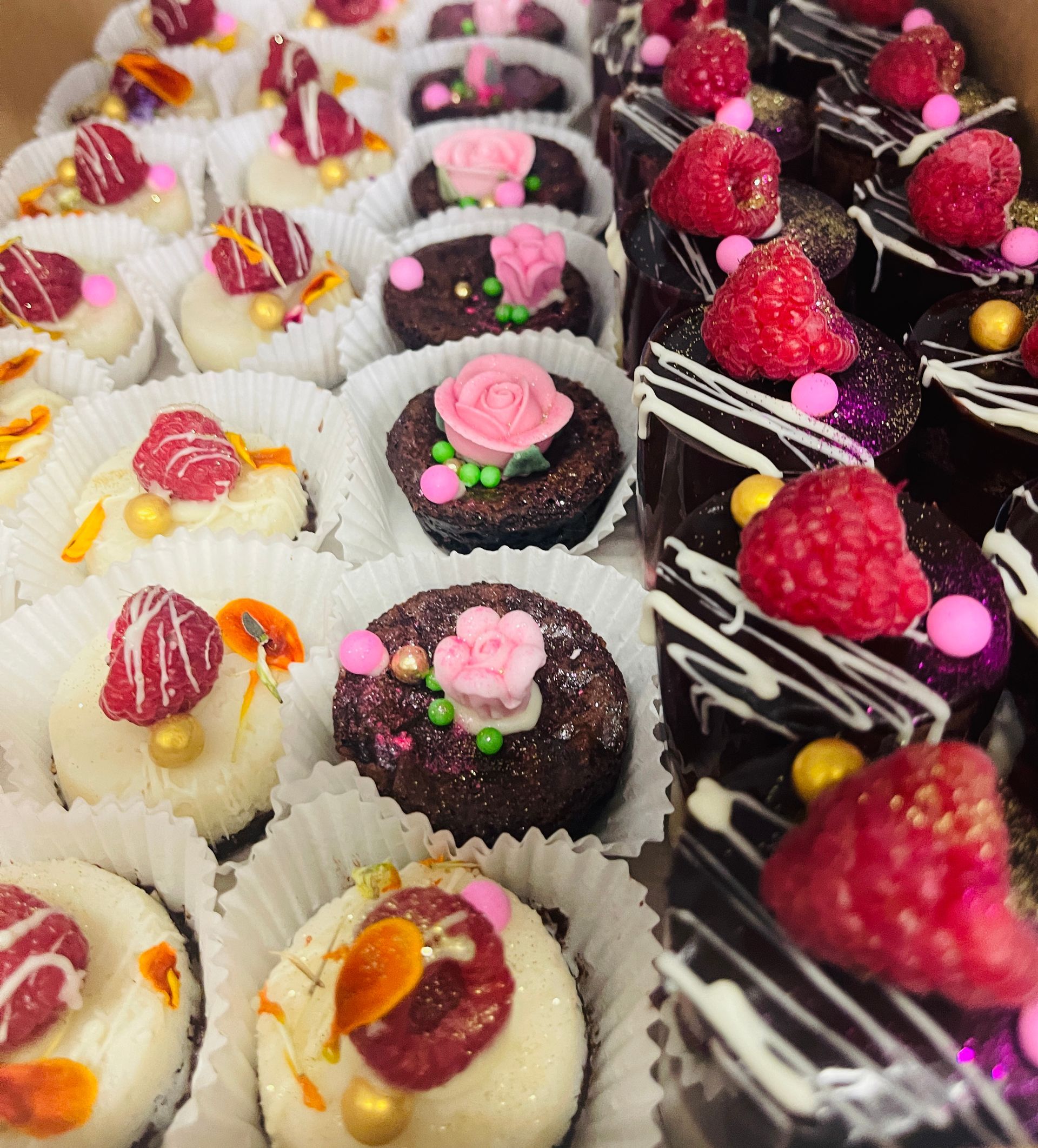 Rows of miniature desserts: white, brown, and chocolate, topped with raspberries, flowers, and decorations — My Rainbow Bakery, Cafe & Catering in Cannonvale, QLD