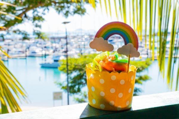 A Box of Food is Sitting on a Table in Front of a Beach — My Rainbow Bakery, Cafe & Catering in Cannonvale, QLD