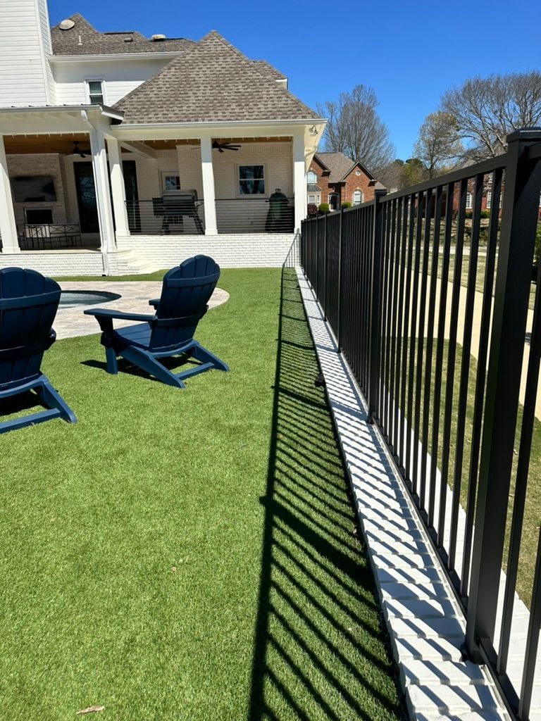 A black fence surrounds a lush green lawn in front of a house.