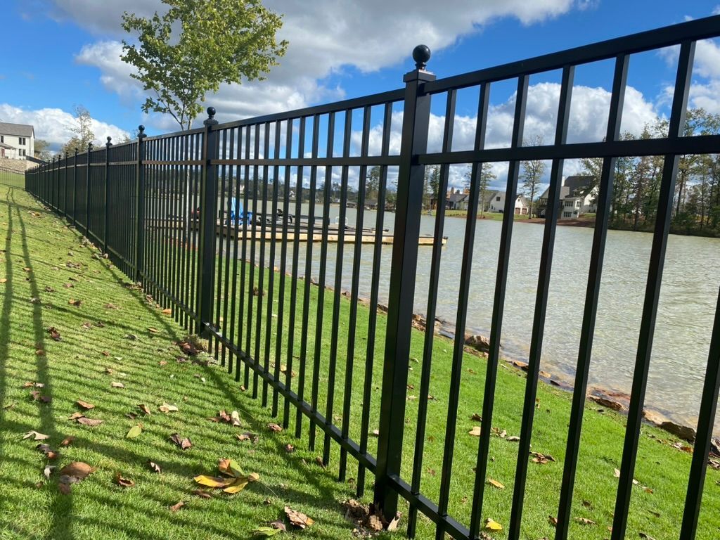 A black metal fence surrounds a grassy area next to a body of water.