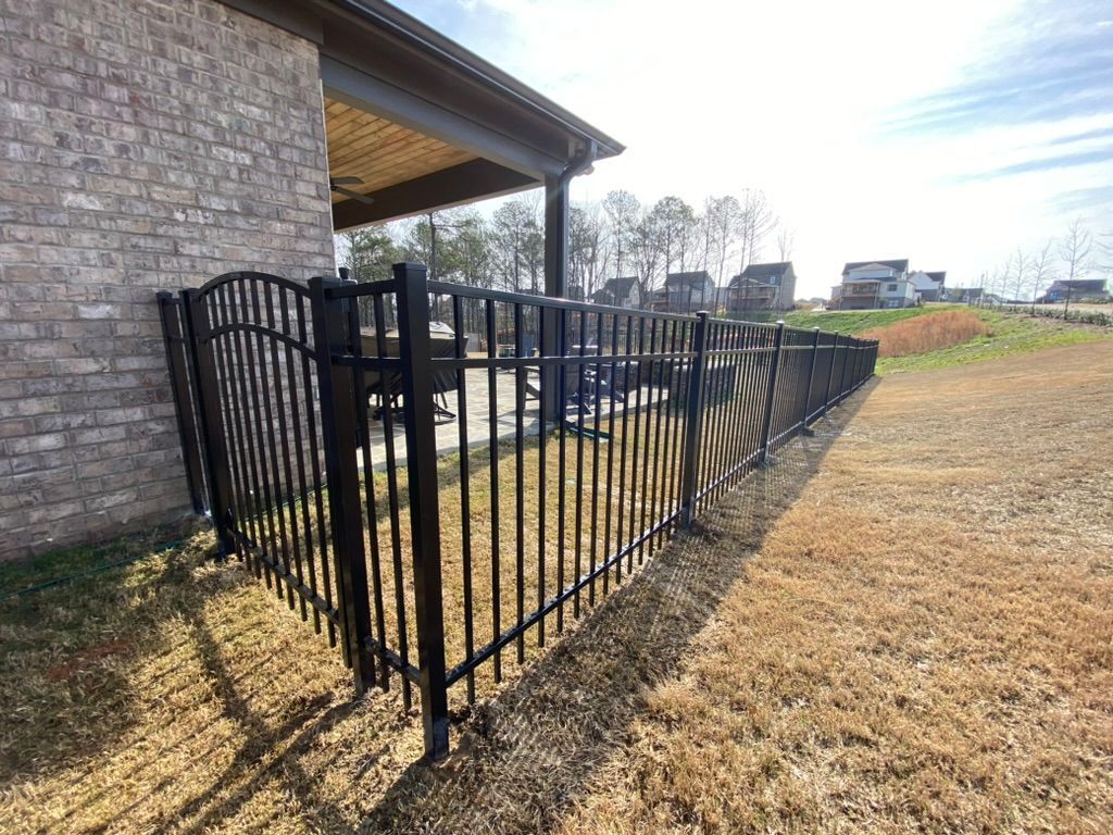 A black fence is surrounding a brick house in a yard.