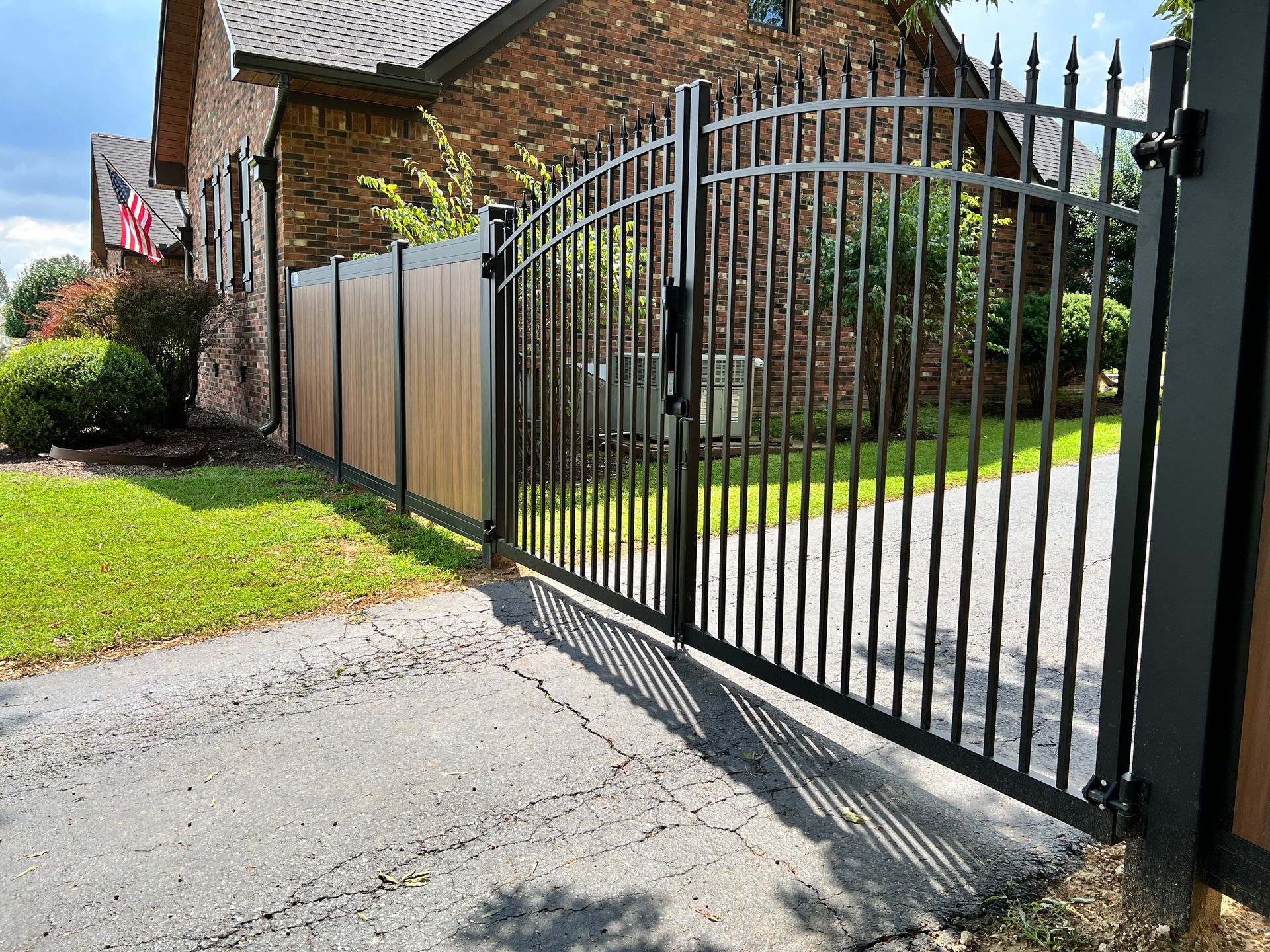 A wrought iron gate is open to a driveway in front of a brick house.