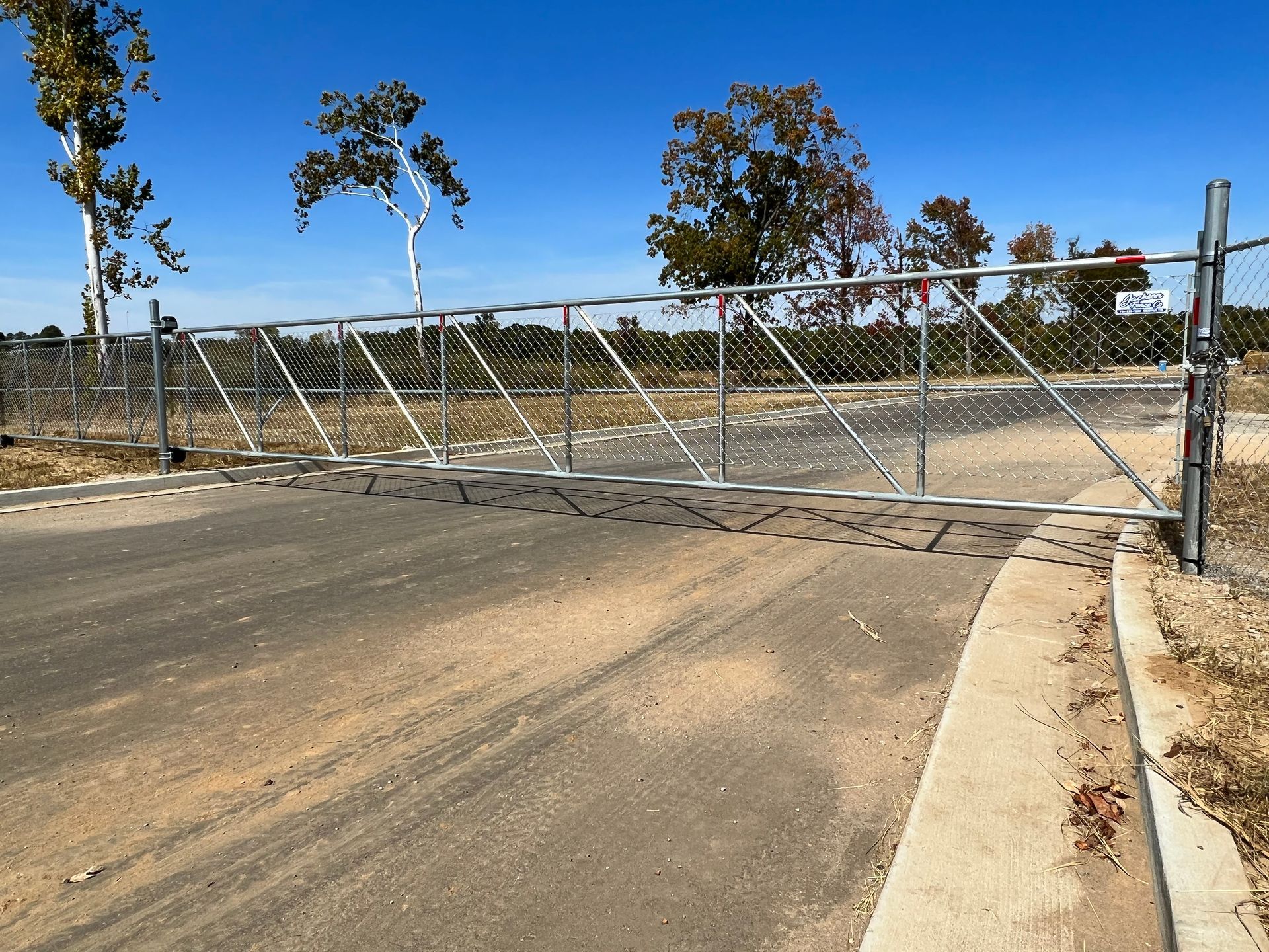 A metal gate is blocking a dirt road with trees in the background.