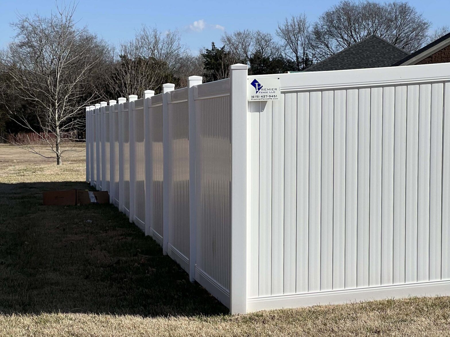 A white vinyl fence is sitting in the middle of a grassy field.