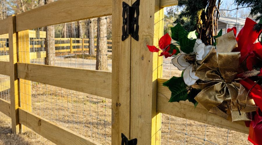 Wooden fence posts joined by black hinges, adorned with a festive holiday wreath featuring red and gold bows.