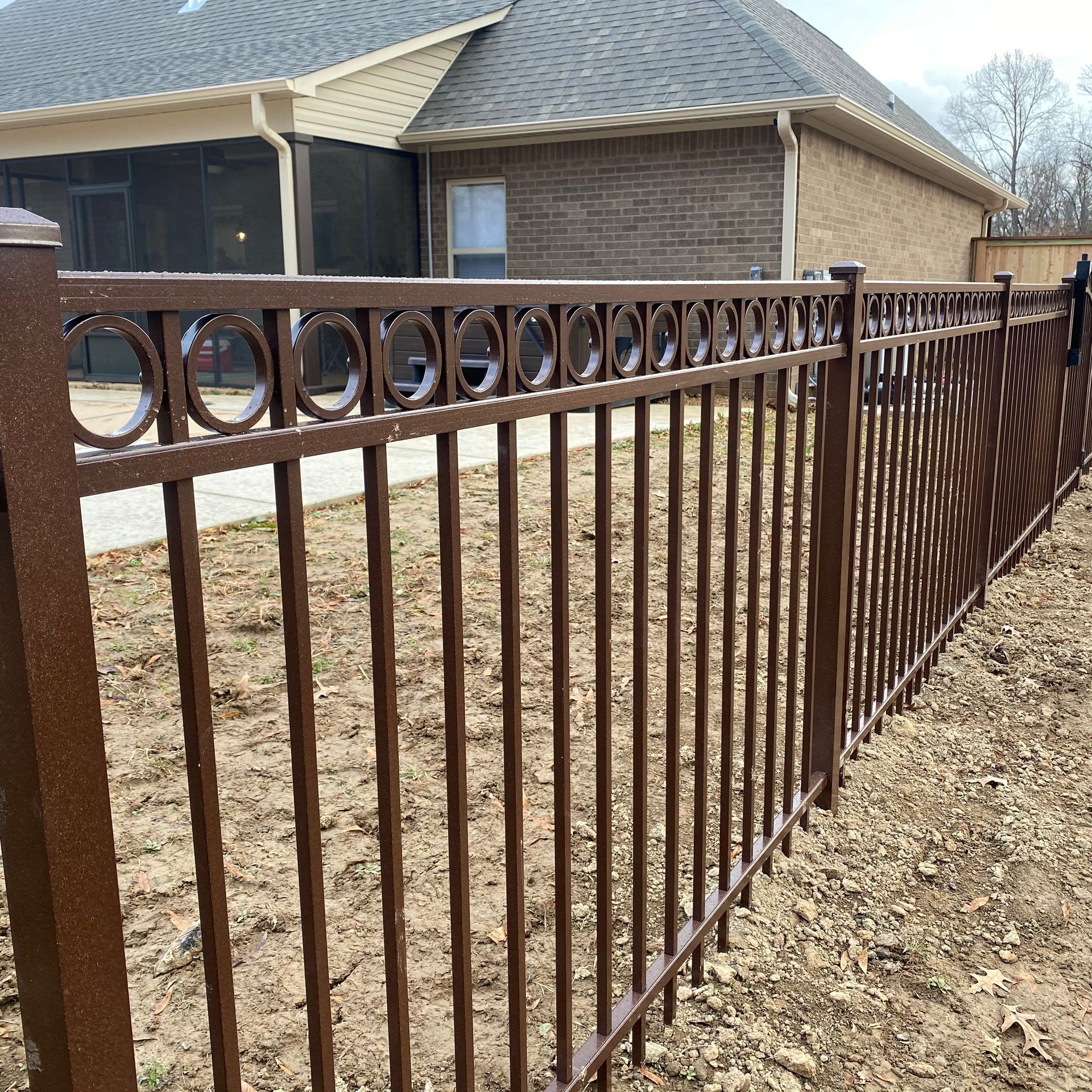 Brown metal fence with circular top design in front of a house.