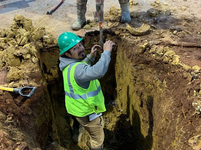 A man in a green hard hat is digging a hole in the dirt.