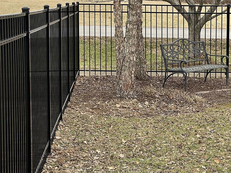 A black fence with a bench in front of it.