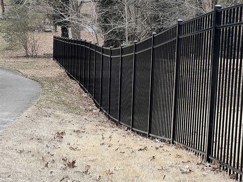 A black metal fence surrounds a driveway in a yard.