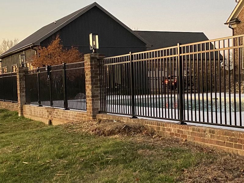 A metal fence surrounds a swimming pool in front of a house.