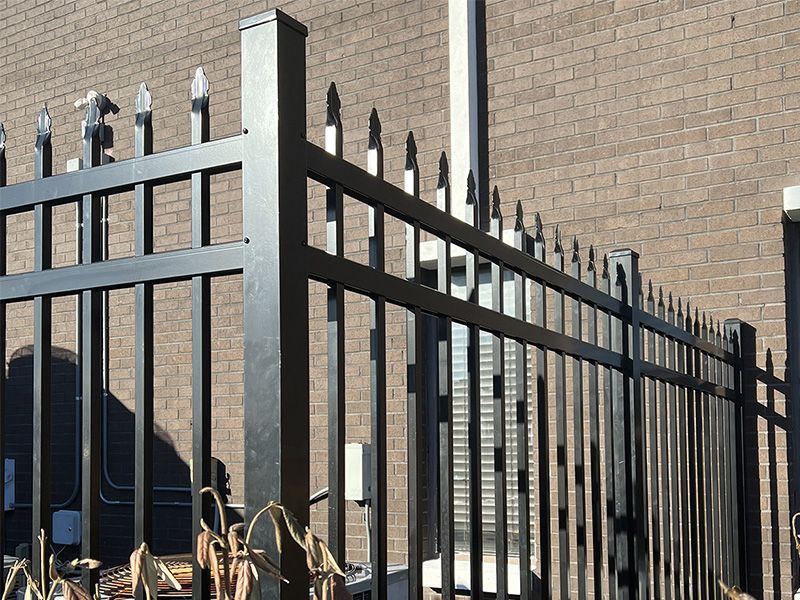 A black metal fence is in front of a brick building.