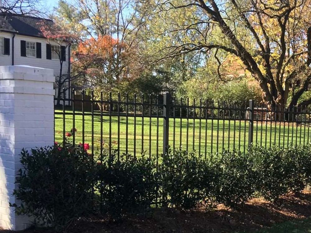 A wrought iron fence surrounds a lush green field in front of a house.